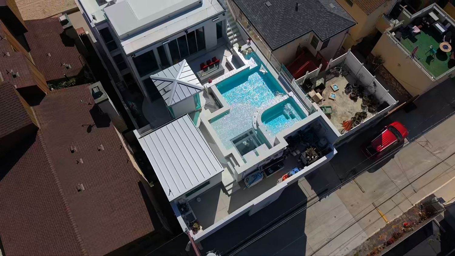 Aerial view of a modern beachside home with a rooftop pool and white deck in a coastal neighborhood.