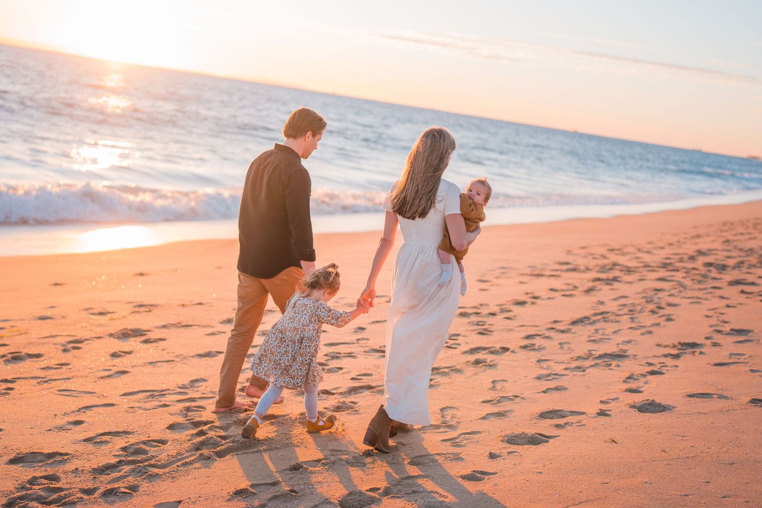 Couple walking together on a sandy beach during golden hour sunset.