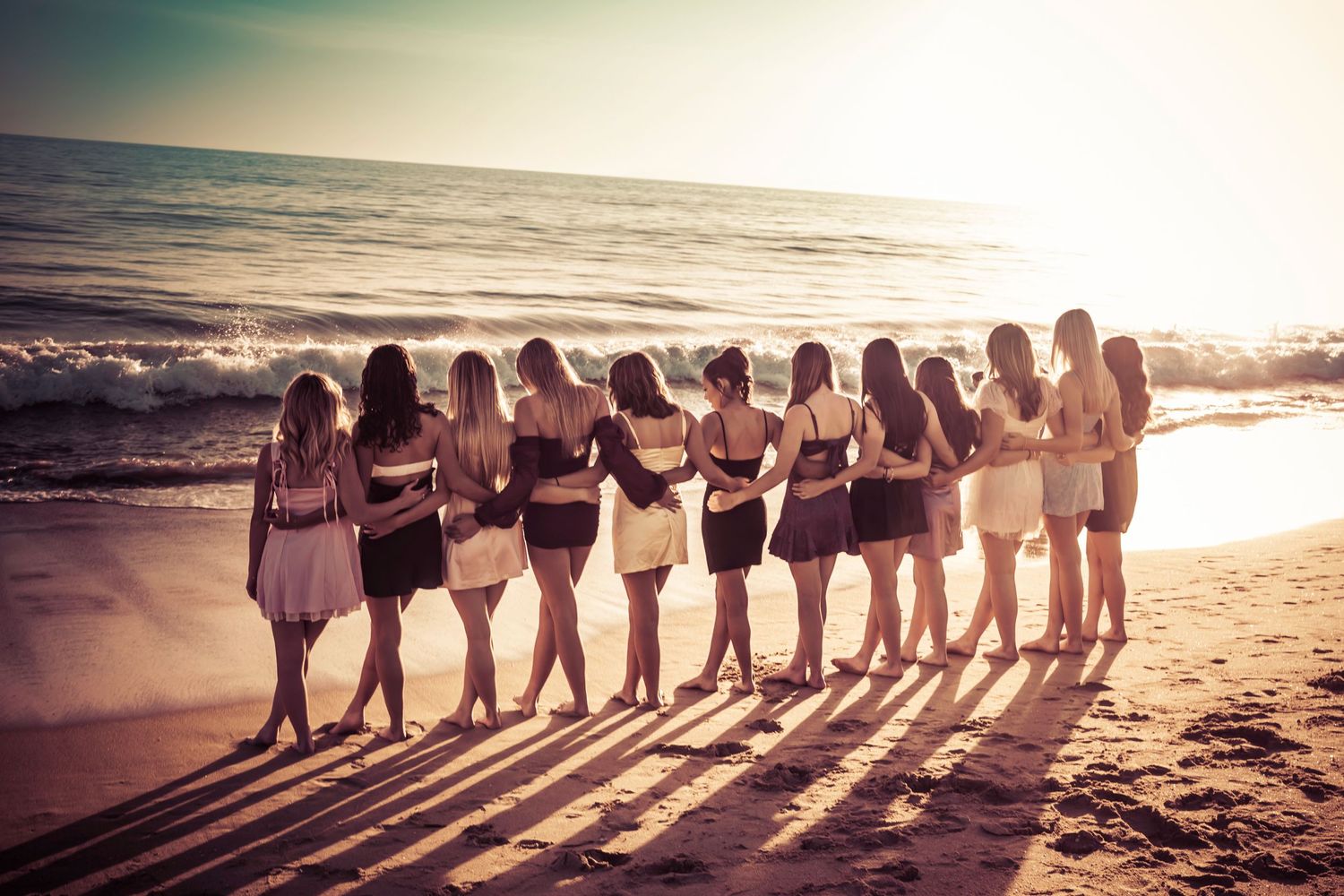 Silhouettes of people lined up on beach at sunset creating long shadows.