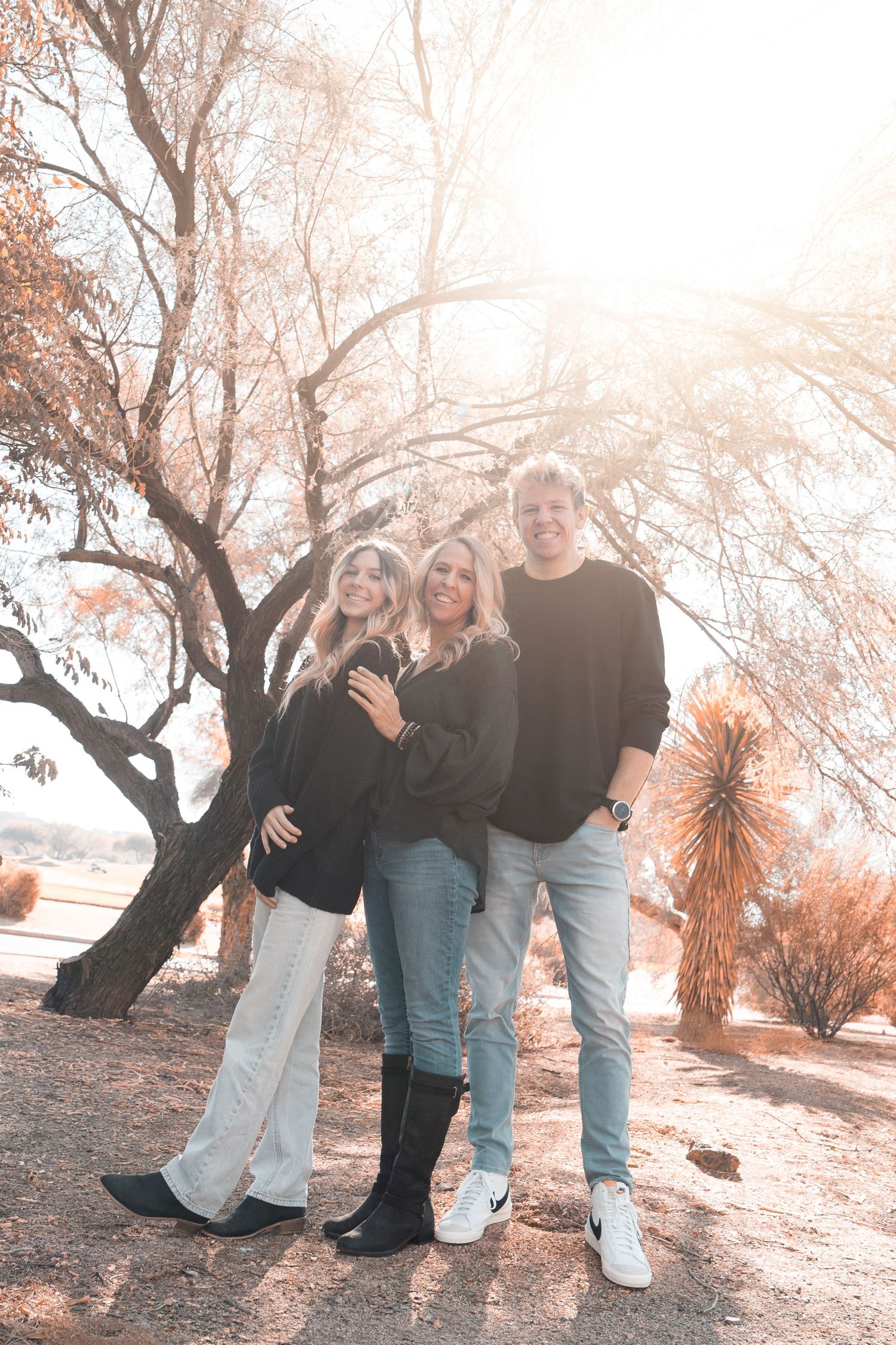 Family posing together in a dreamy autumn setting with soft pink tones and trees in the background.