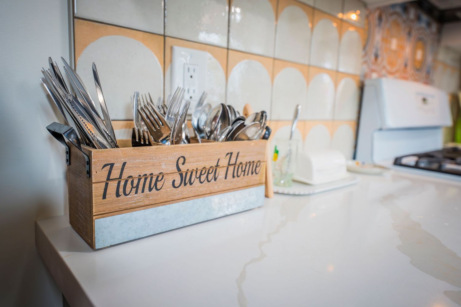 Wooden 'Home Sweet Home' utensil holder with silverware on a white marble kitchen countertop.