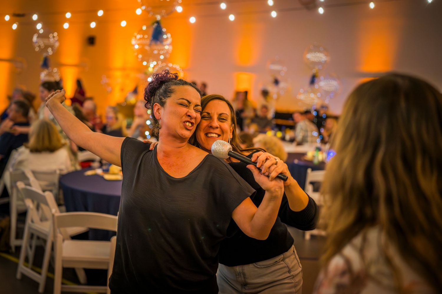 People dancing and celebrating at a lively reception with warm orange lighting and decorations.