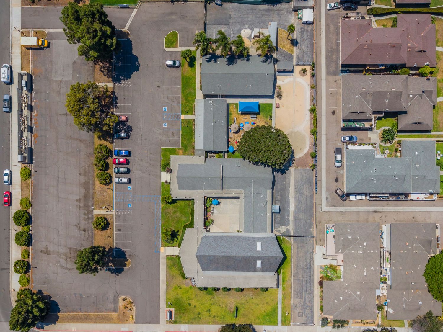 Aerial top-down view of a residential neighborhood with buildings, parking lots, and green trees in a suburban area.