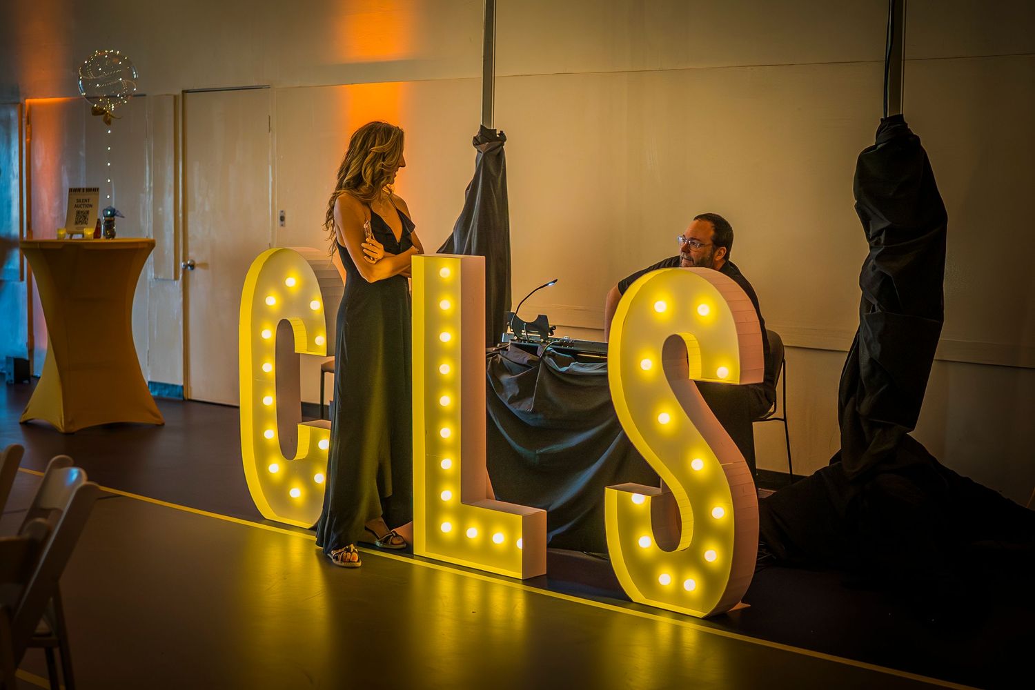 Large illuminated CLS letters with woman in black dress making request to the DJ.