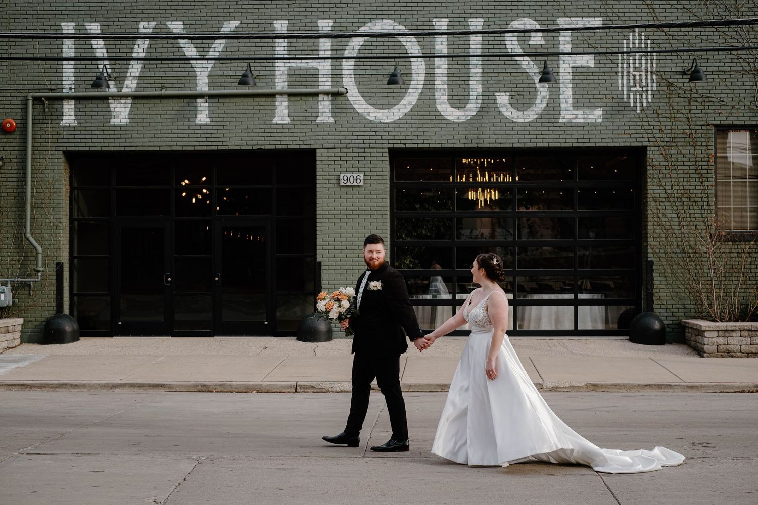 Bride and groom walking hand in hand infant of their venue, with the bride’s dress flowing gracefully and the groom smiling at her