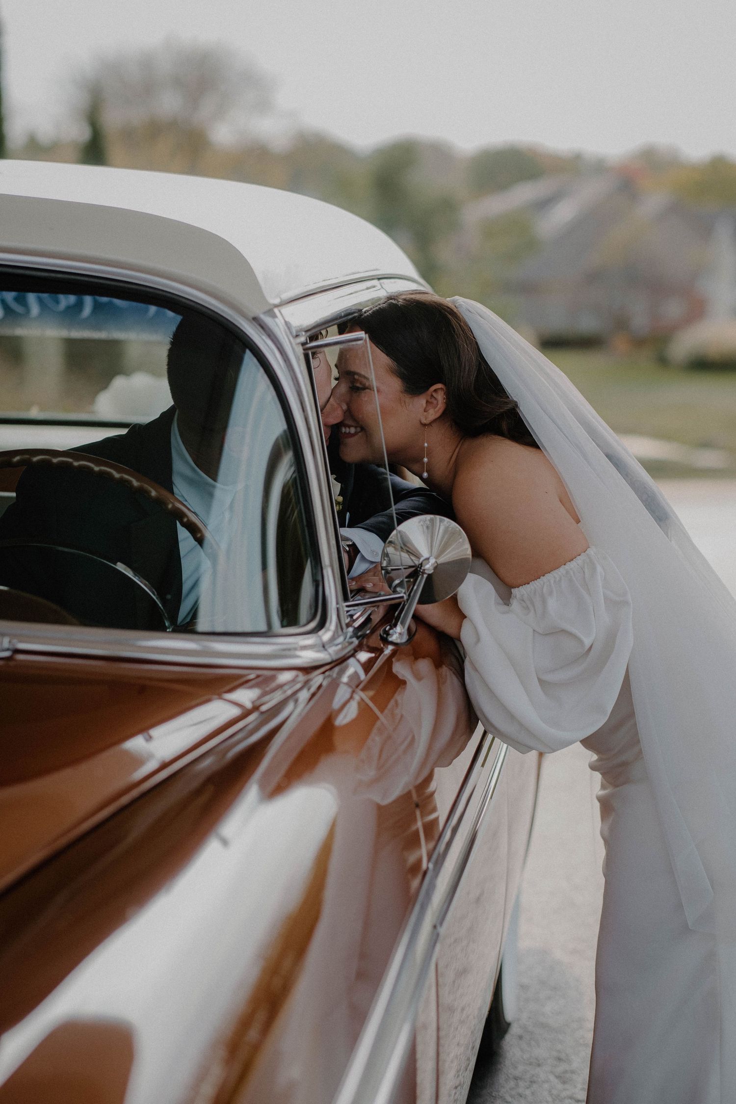 Bride and groom sharing a romantic kiss inside a vintage car, with the bride’s veil gently flowing and the soft glow of the car’s interior
