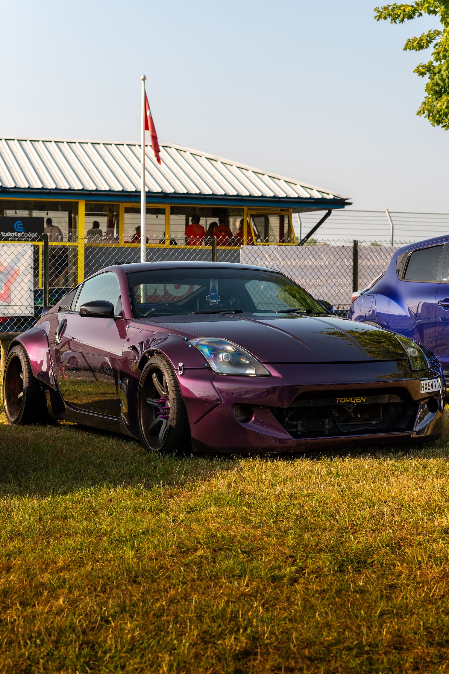A modified purple Nissan 370Z with wide body kit parked on grass at a car show event.