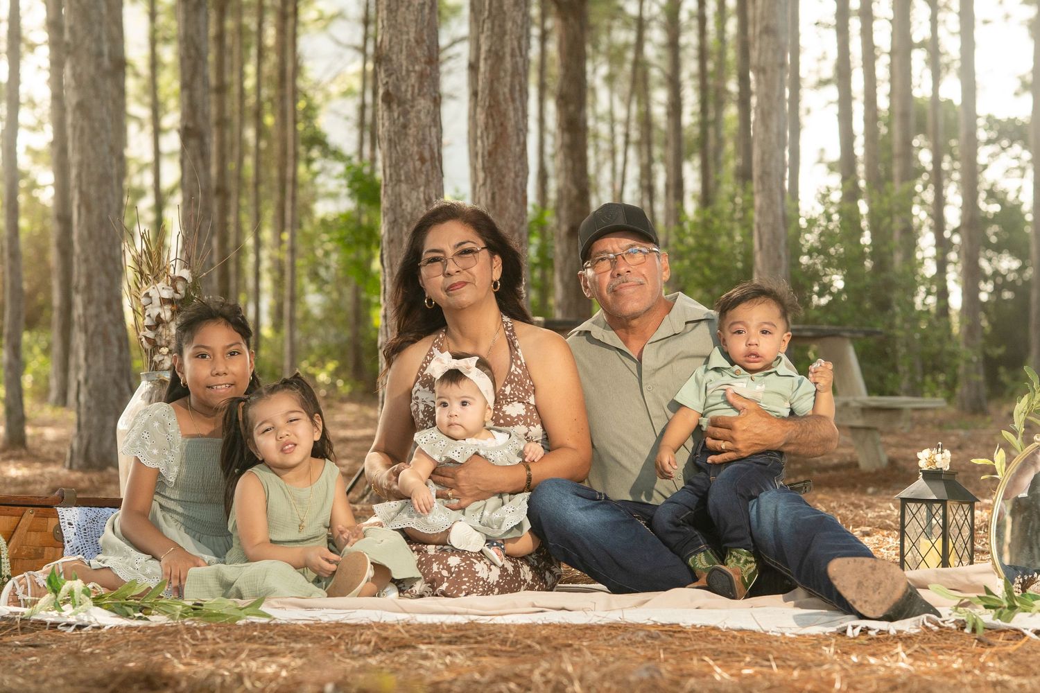Family of five posing outdoors among tall pine trees, including grandparents and three young children on a blanket.