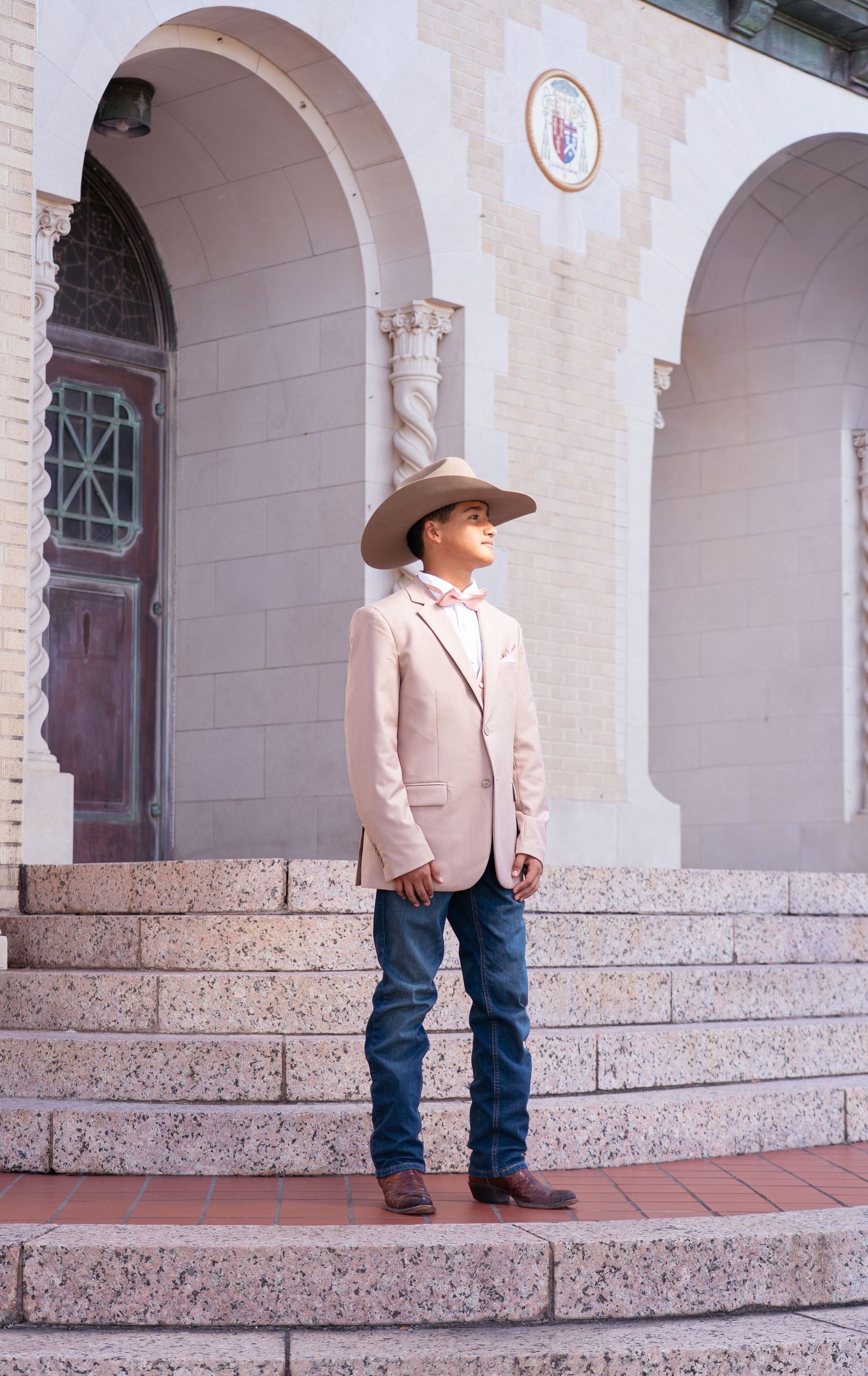A person in western attire stands alone on stone steps against a classical architectural backdrop.