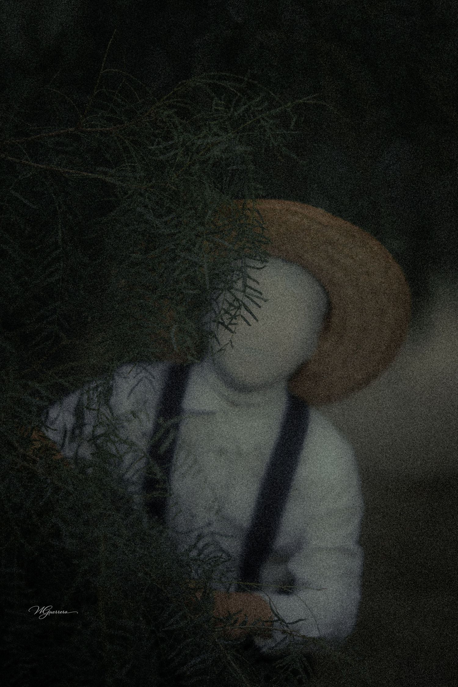 A faceless figure in a straw hat and suspenders holds wild greenery in a dark, eerie artistic photograph.