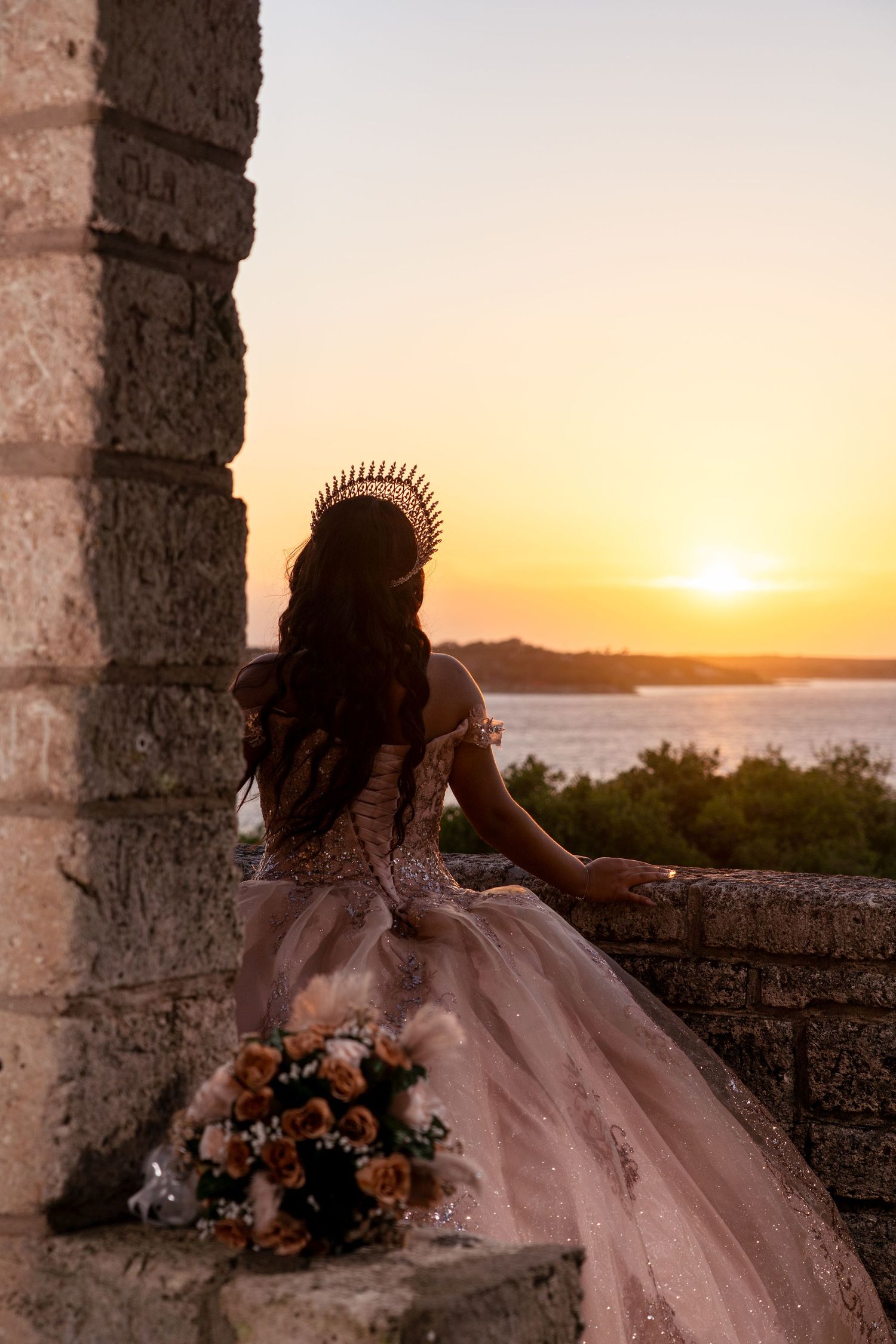A quinceañera dress photoshoot at sunset featuring a flowing pink ballgown and floral bouquet.