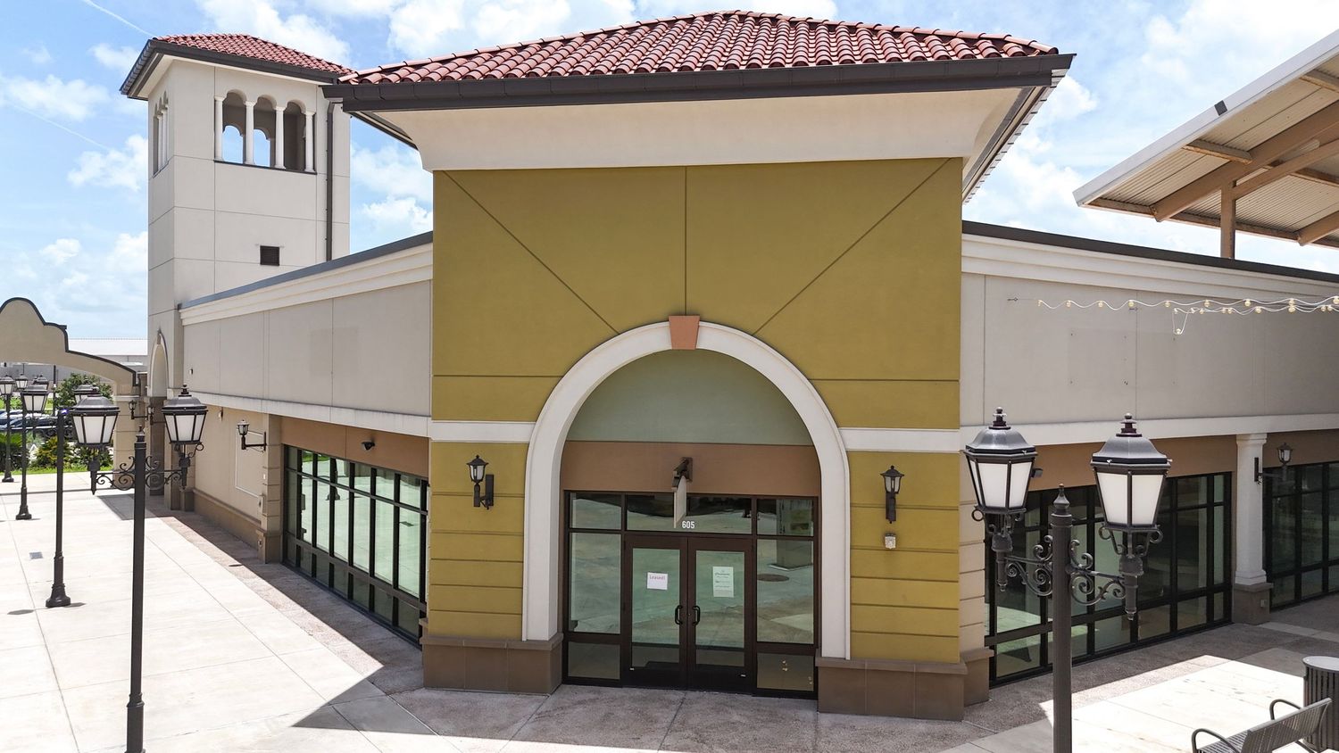 A panoramic view of a Mediterranean-style shopping plaza with terracotta roofs and yellow stucco walls.
