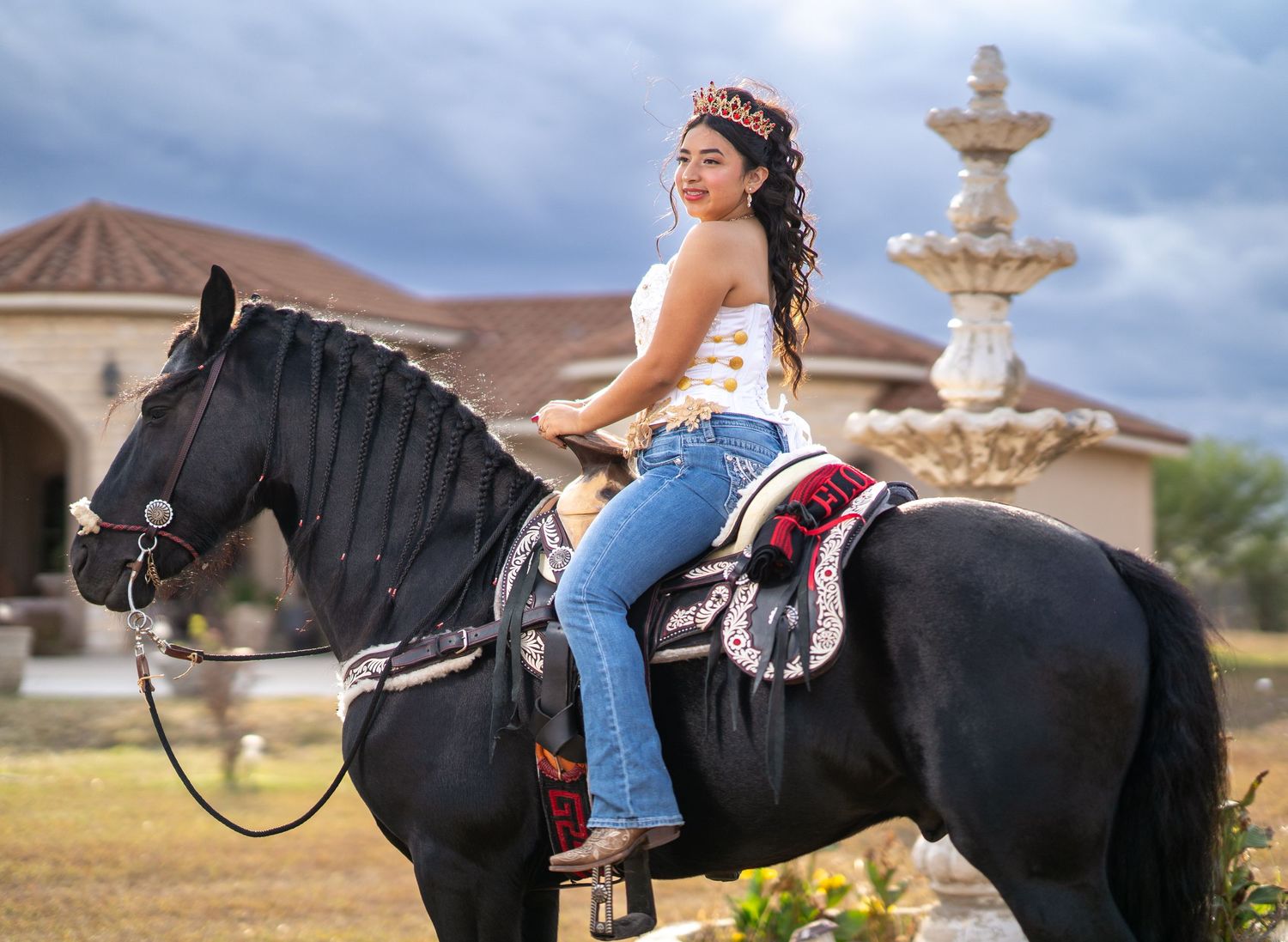 A decorated black horse stands near a stone fountain in an outdoor setting.