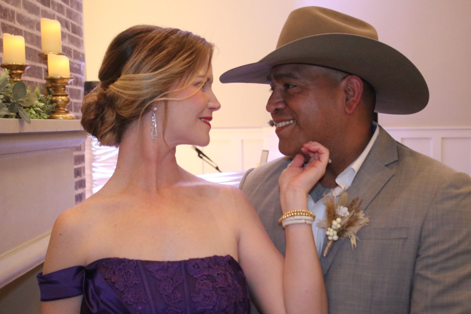 A romantic moment between two people at an indoor event with candles in the background.