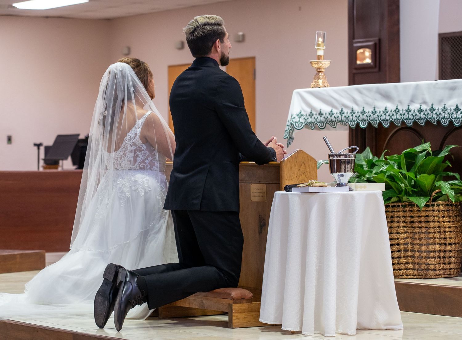 A wedding couple sits at a table with white tablecloths in an elegant reception venue.