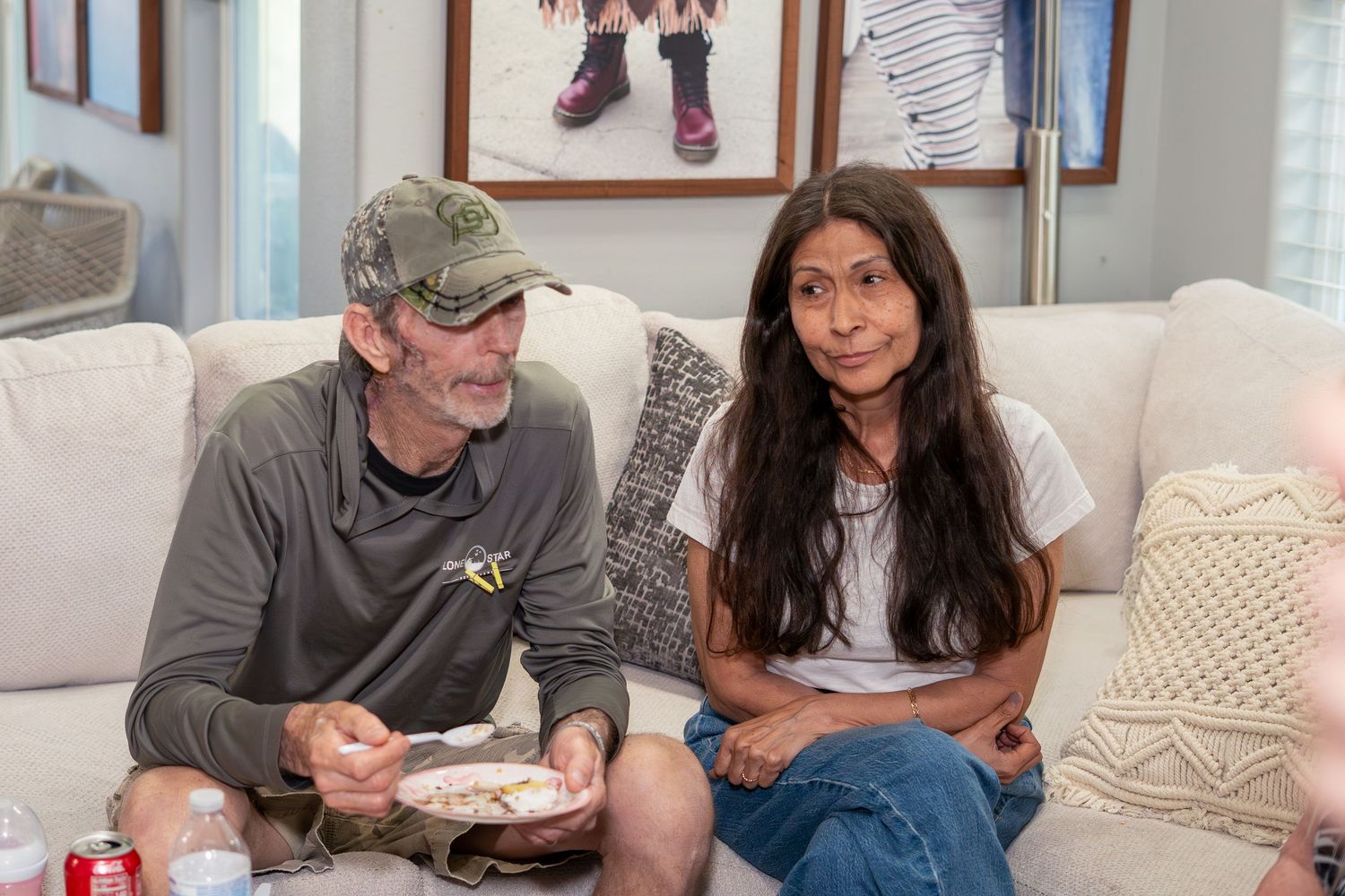 A man and woman sitting together on a white couch, sharing a meal in a cozy living room setting.