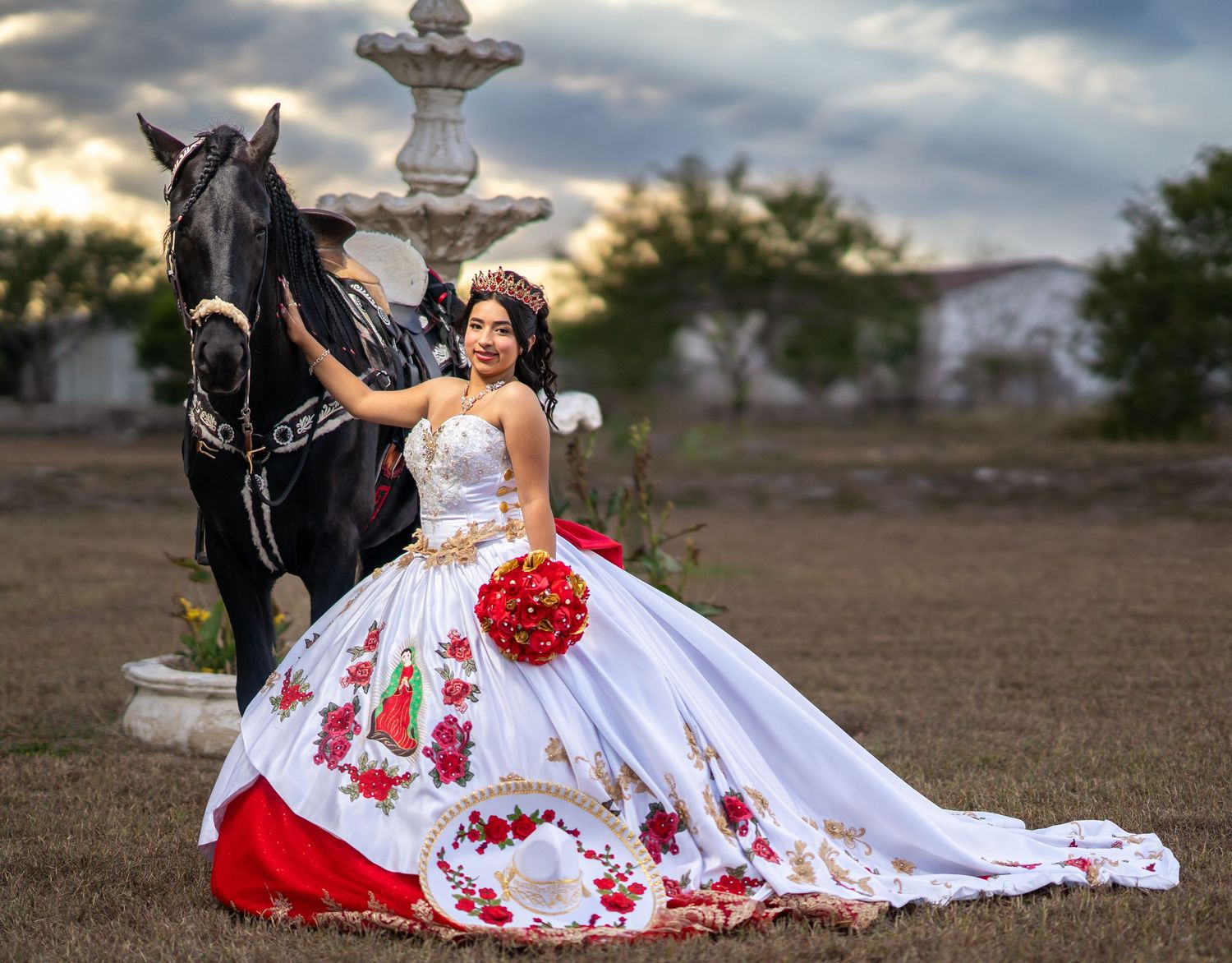 Beautiful quinceañera photoshoot featuring a white dress with red accents and a black horse in an open field.