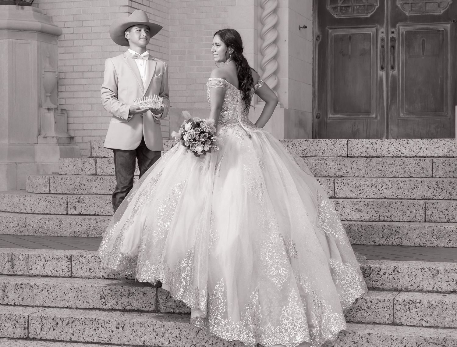 A black and white wedding photograph showing a couple on stone steps with the bride wearing a voluminous lace gown.
