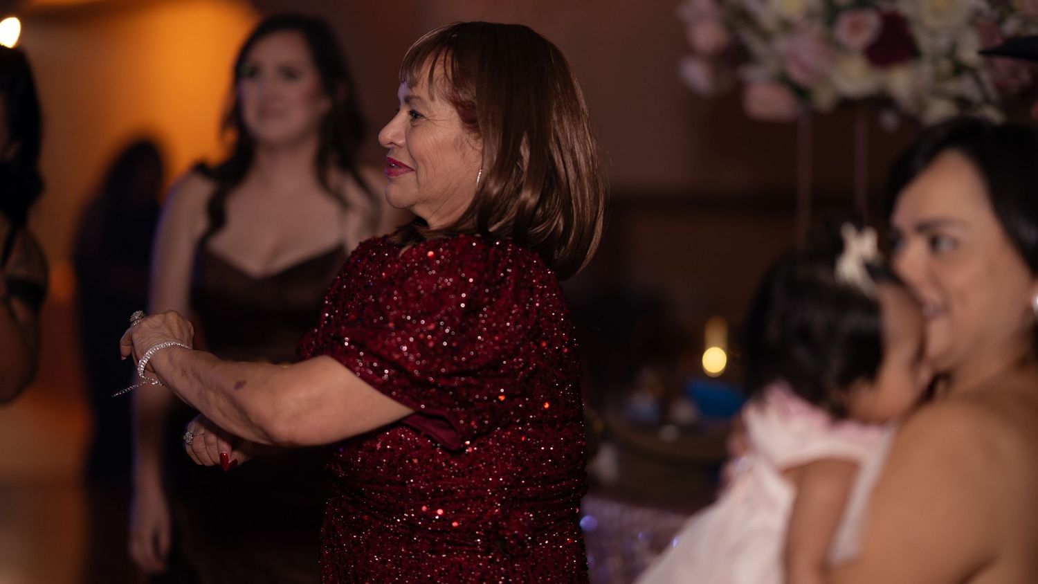 Woman in red sequin dress dances joyfully at an elegant quinceañera celebration event.