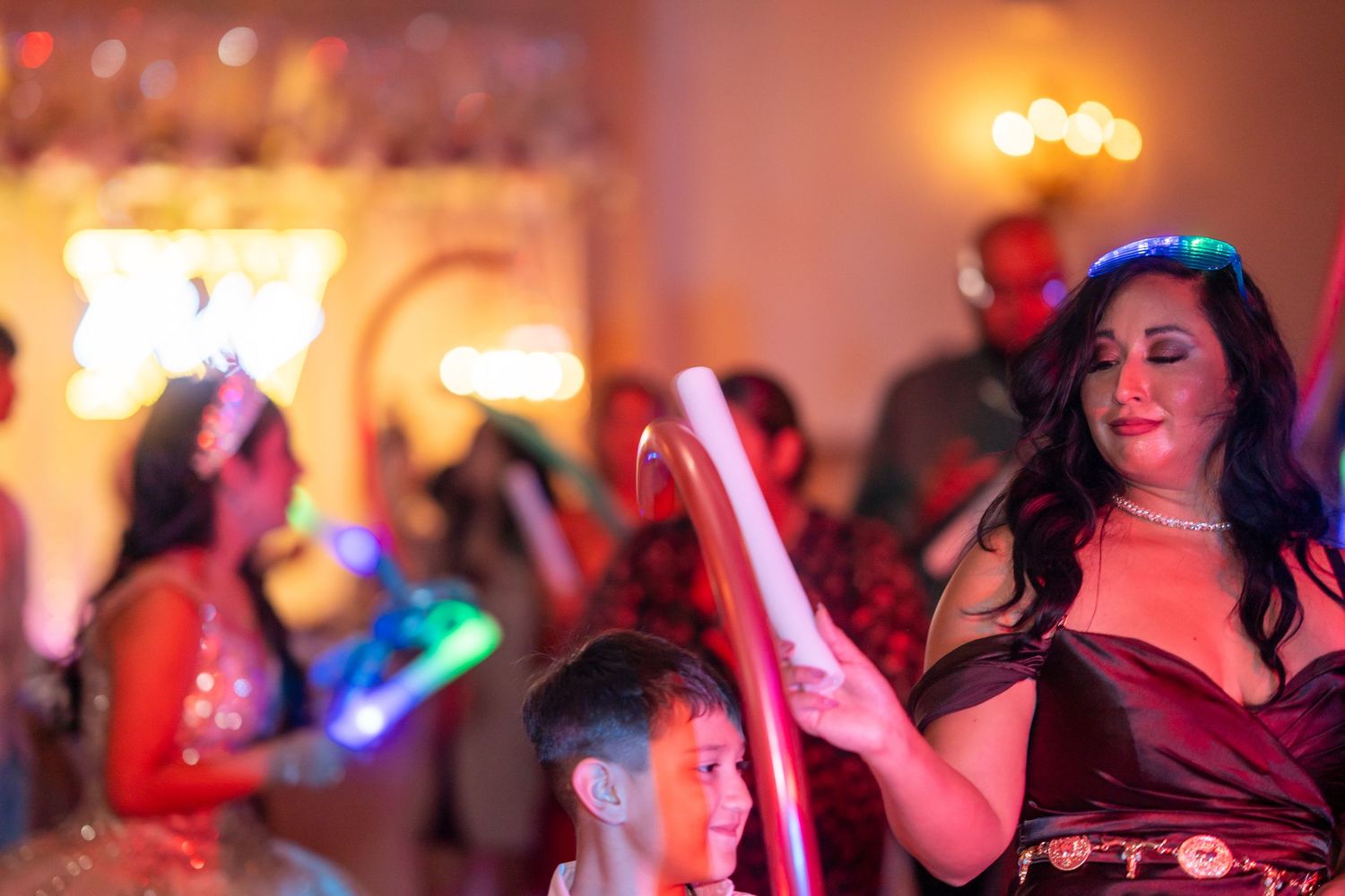 Guests celebrate with glowing light-up accessories and wands on a vibrant, colorful quinceañera dance floor at night.