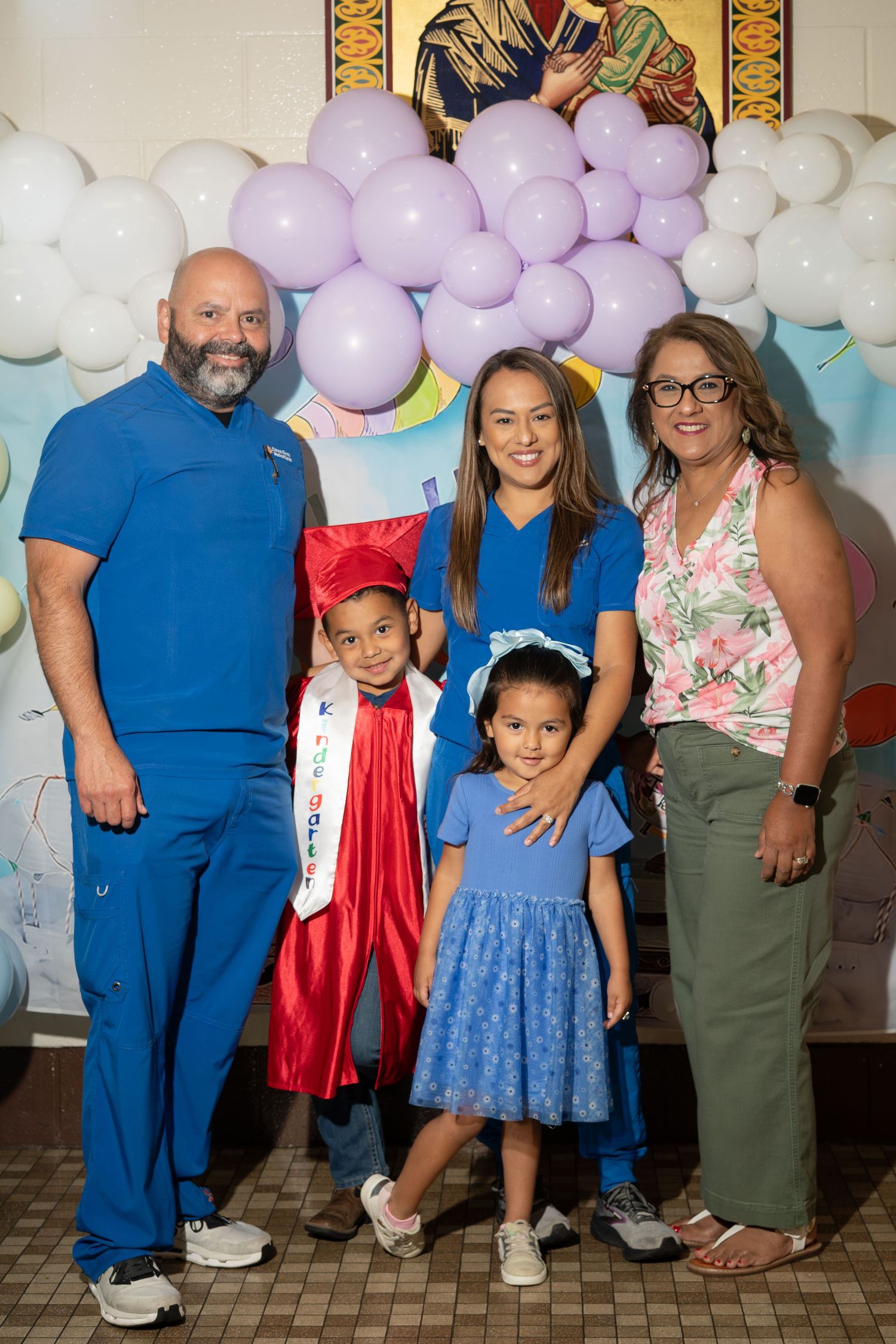 Family of five posing together at a kindergarten graduation celebration with balloon arch backdrop.
