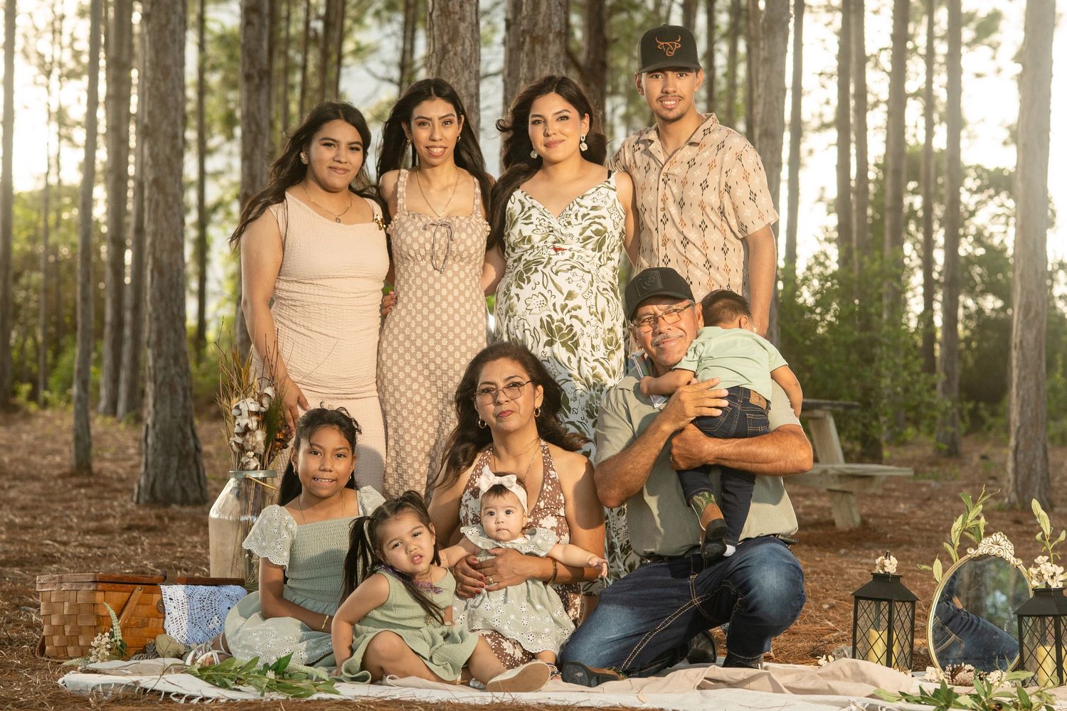 A large Hispanic family poses together outdoors in a pine forest for a professional portrait session.