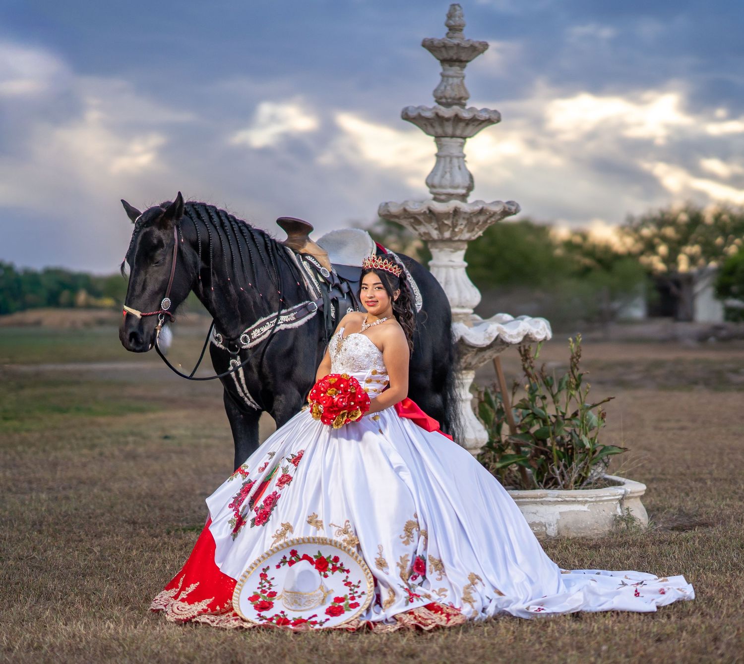 Elegant white and red traditional dress with a black horse and decorative stone fountain in the background.