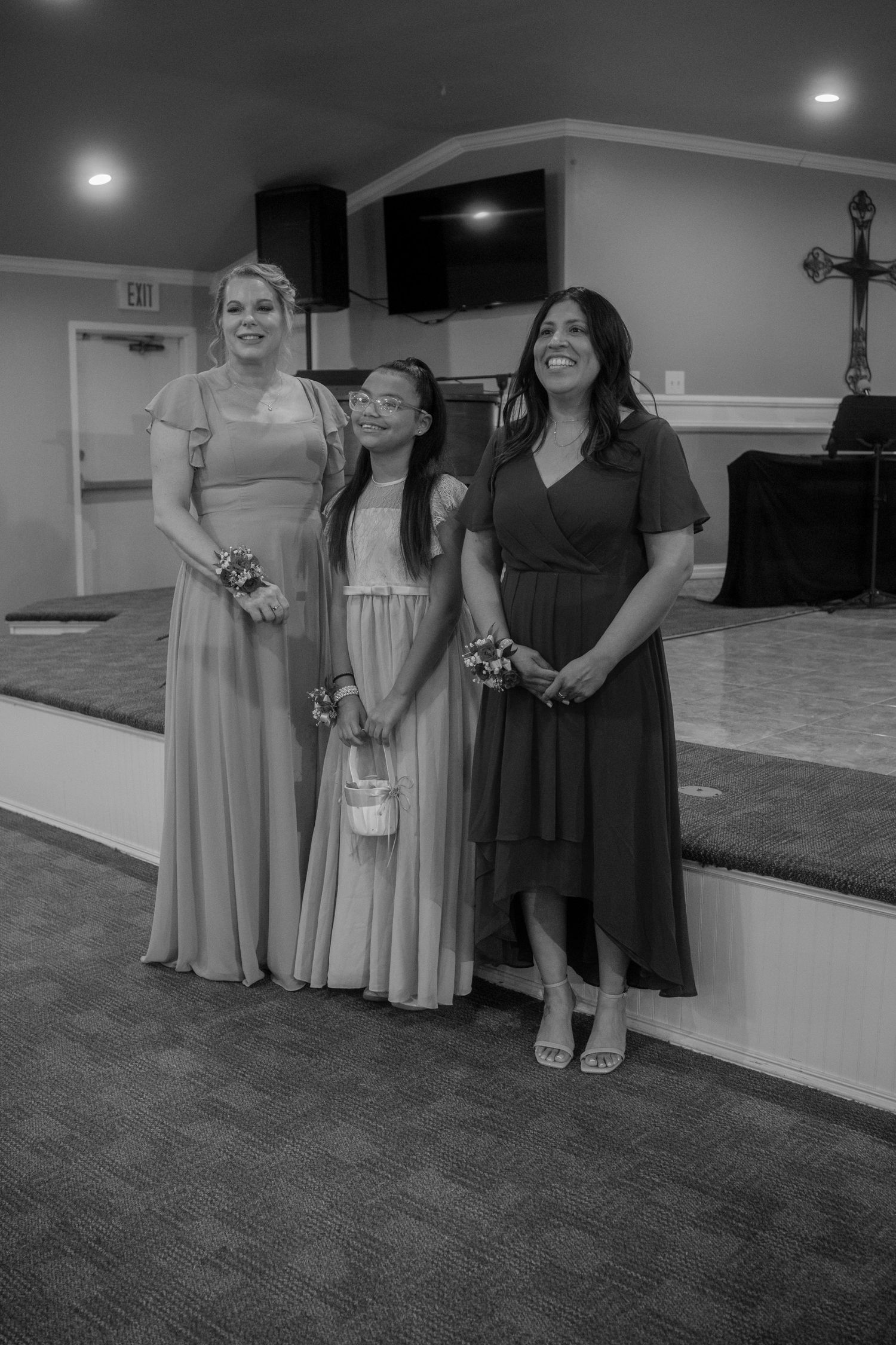 Black and white photo of three bridesmaids in formal dresses posing together inside a wedding venue.