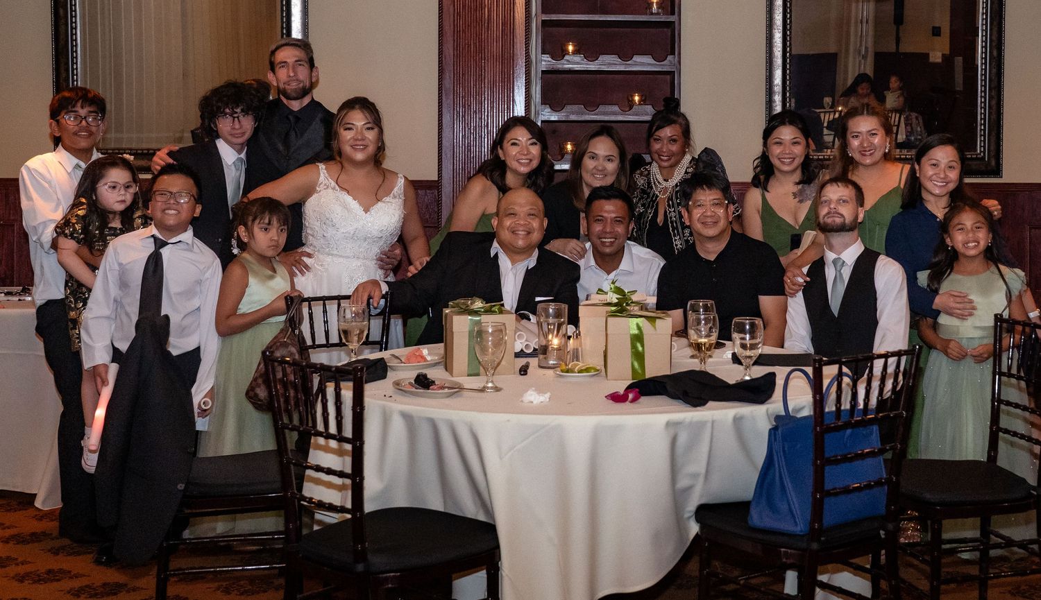 A large wedding party group poses together around a decorated table at an elegant reception venue.