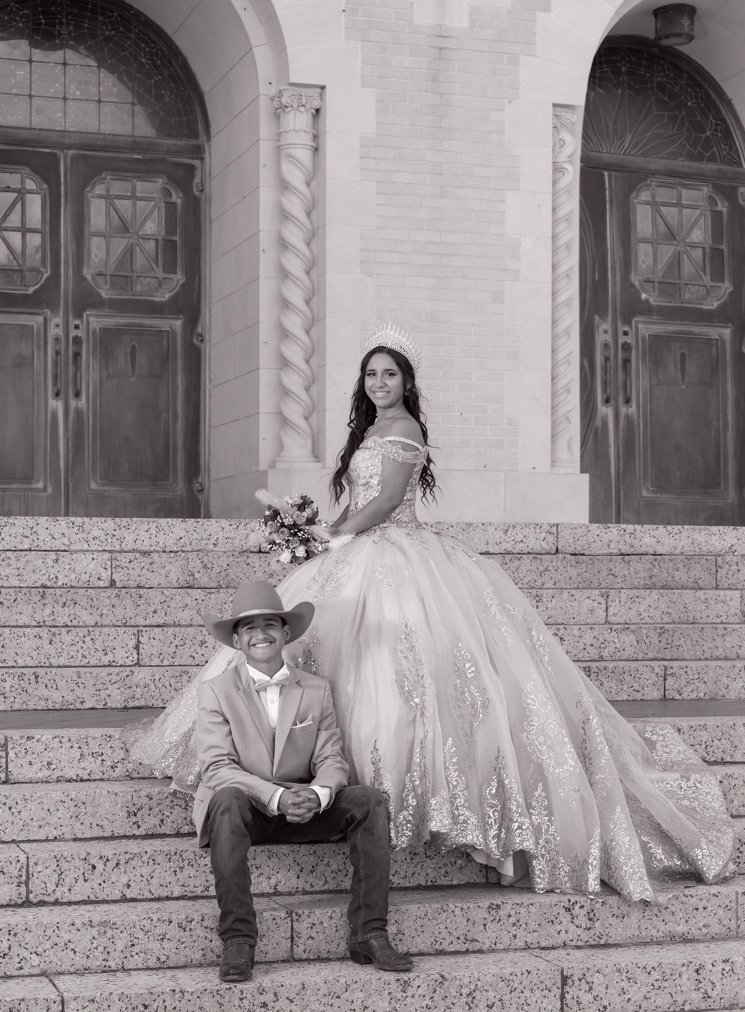 A couple in formal attire poses on stone steps outside a historic building with elegant architecture.