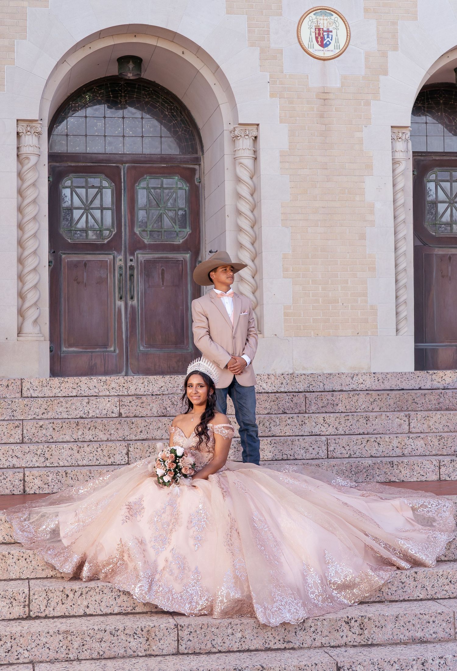 Couple in formal attire poses on stone steps with bride wearing flowing pink ballgown dress.