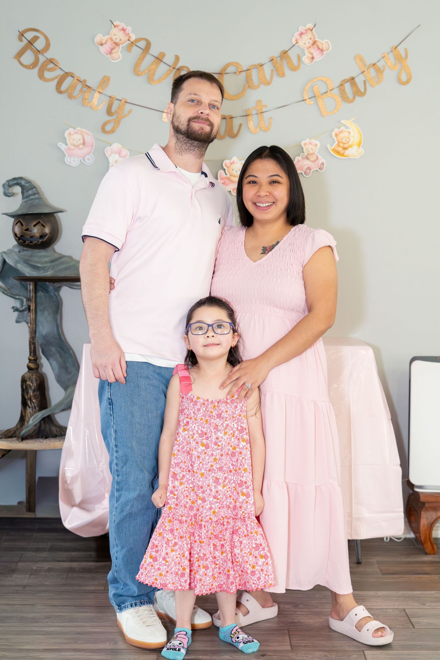 Family of three posing at a baby shower, with gold banner reading We Can Bearly Wait Baby on the wall.