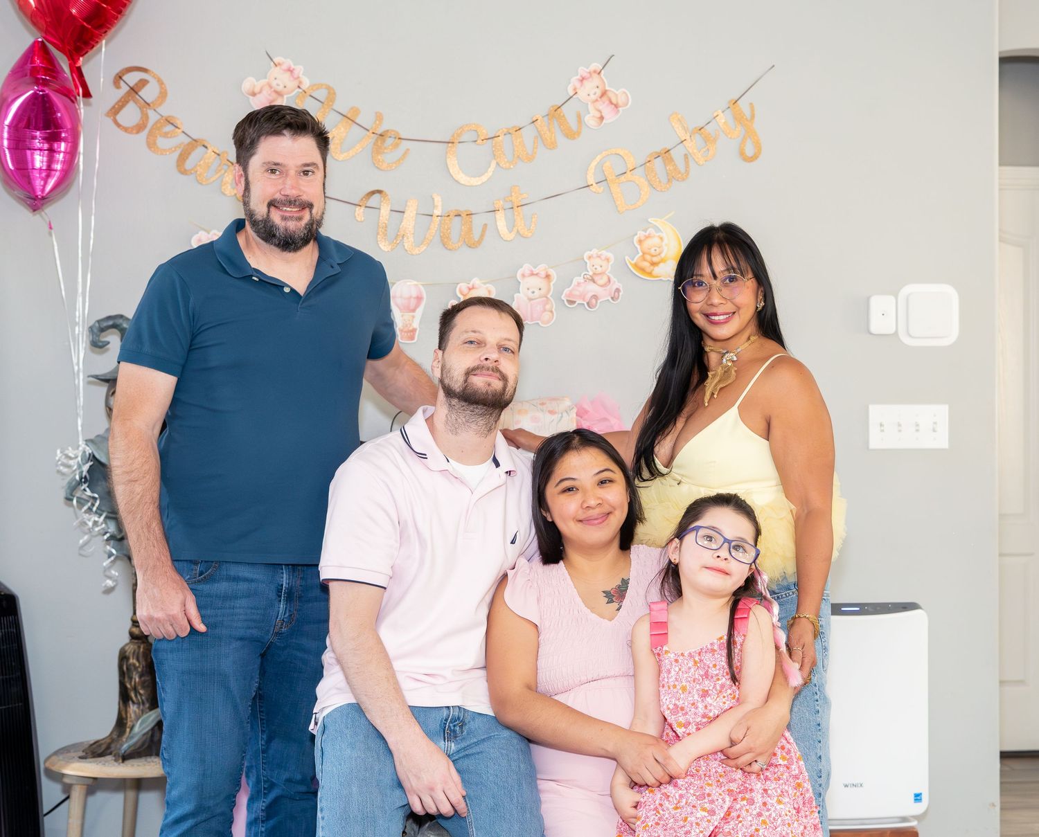 Family of five posing together at a birthday party with balloons and festive banner backdrop.