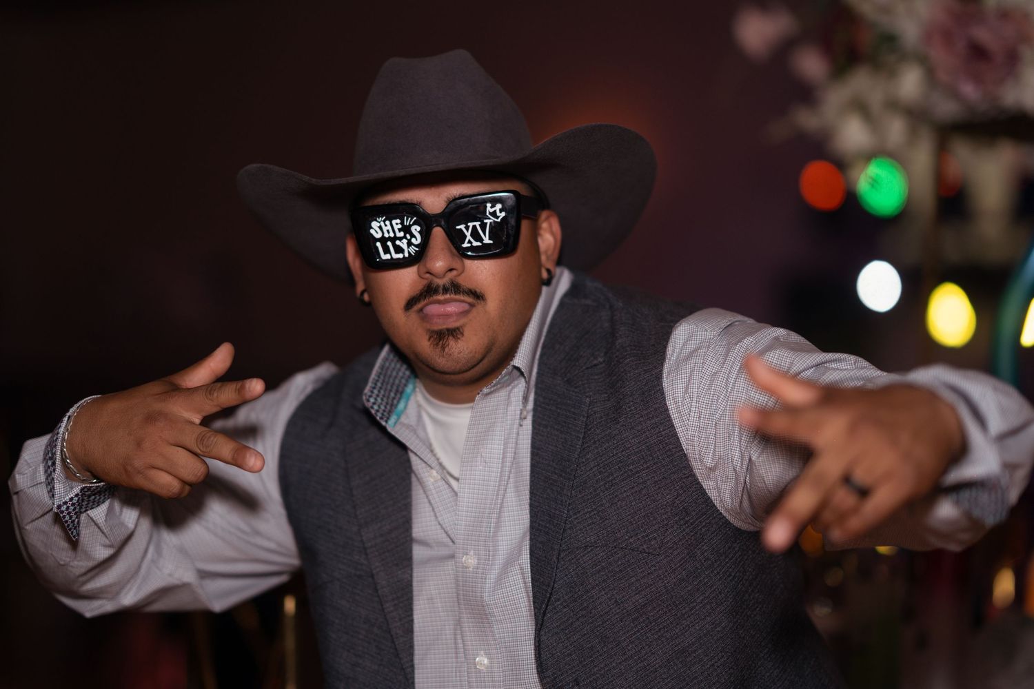 Man in cowboy hat and novelty sunglasses poses at a festive quinceañera party celebration.