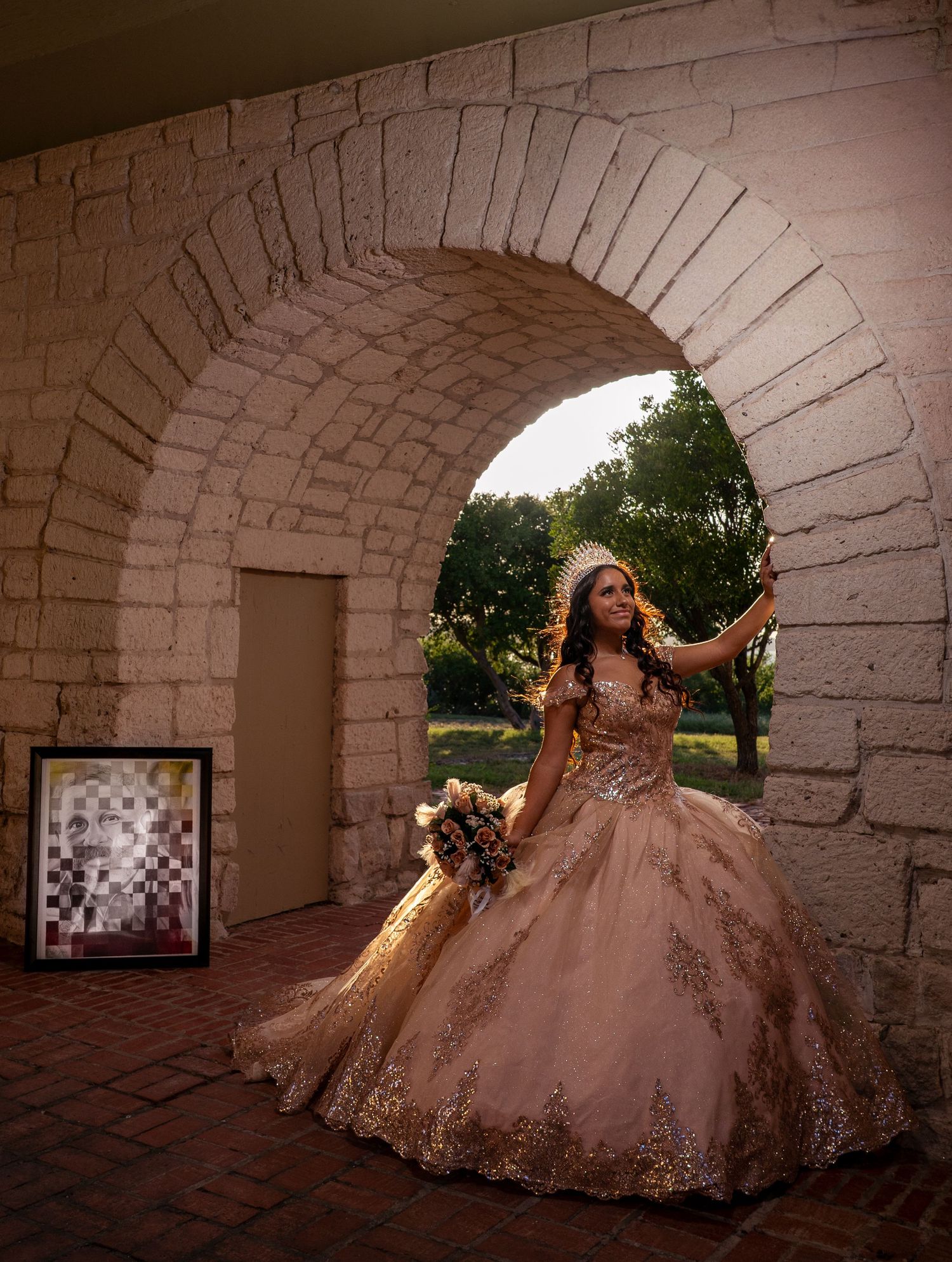 A stunning quinceanera dress photoshoot features a teen in a sparkling rose gold gown under stone archways.