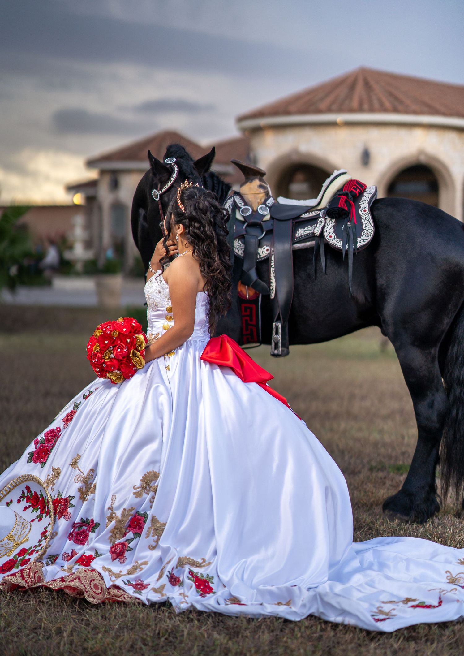 Elegant quinceañera dress with red floral embroidery photographed with a black horse in an open field.