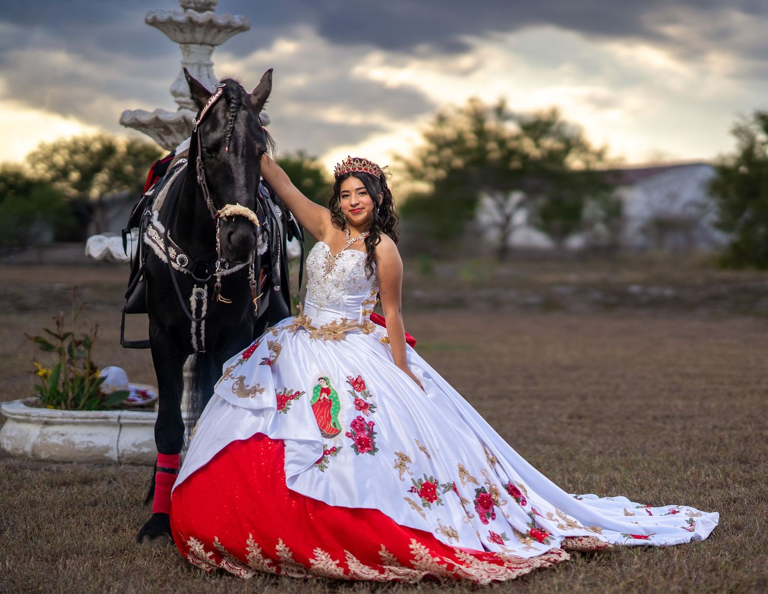 A dramatic sunset photo shoot featuring a white and red quinceañera dress with a black horse in a field.