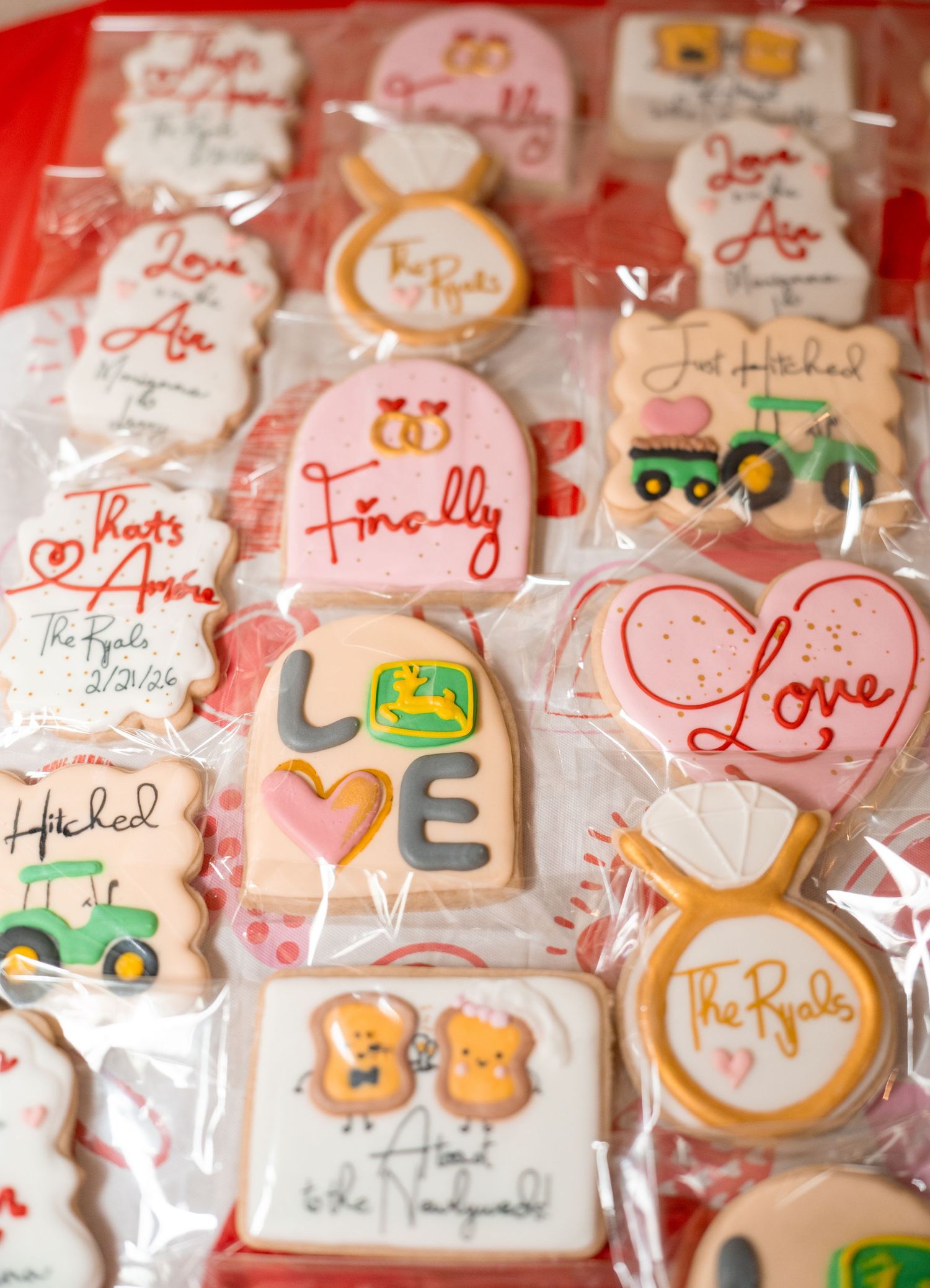 Assorted wedding-themed decorated sugar cookies with love messages, rings, and John Deere tractor designs for The Ryals.