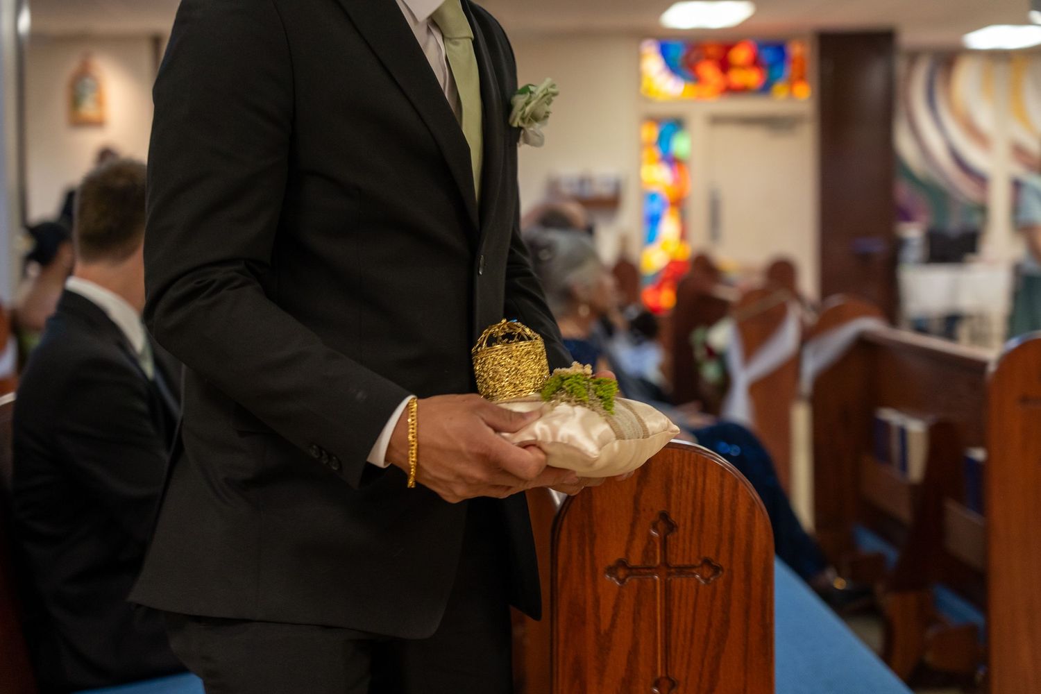 Groom holding wedding rings on a pillow in a church aisle during a wedding ceremony.