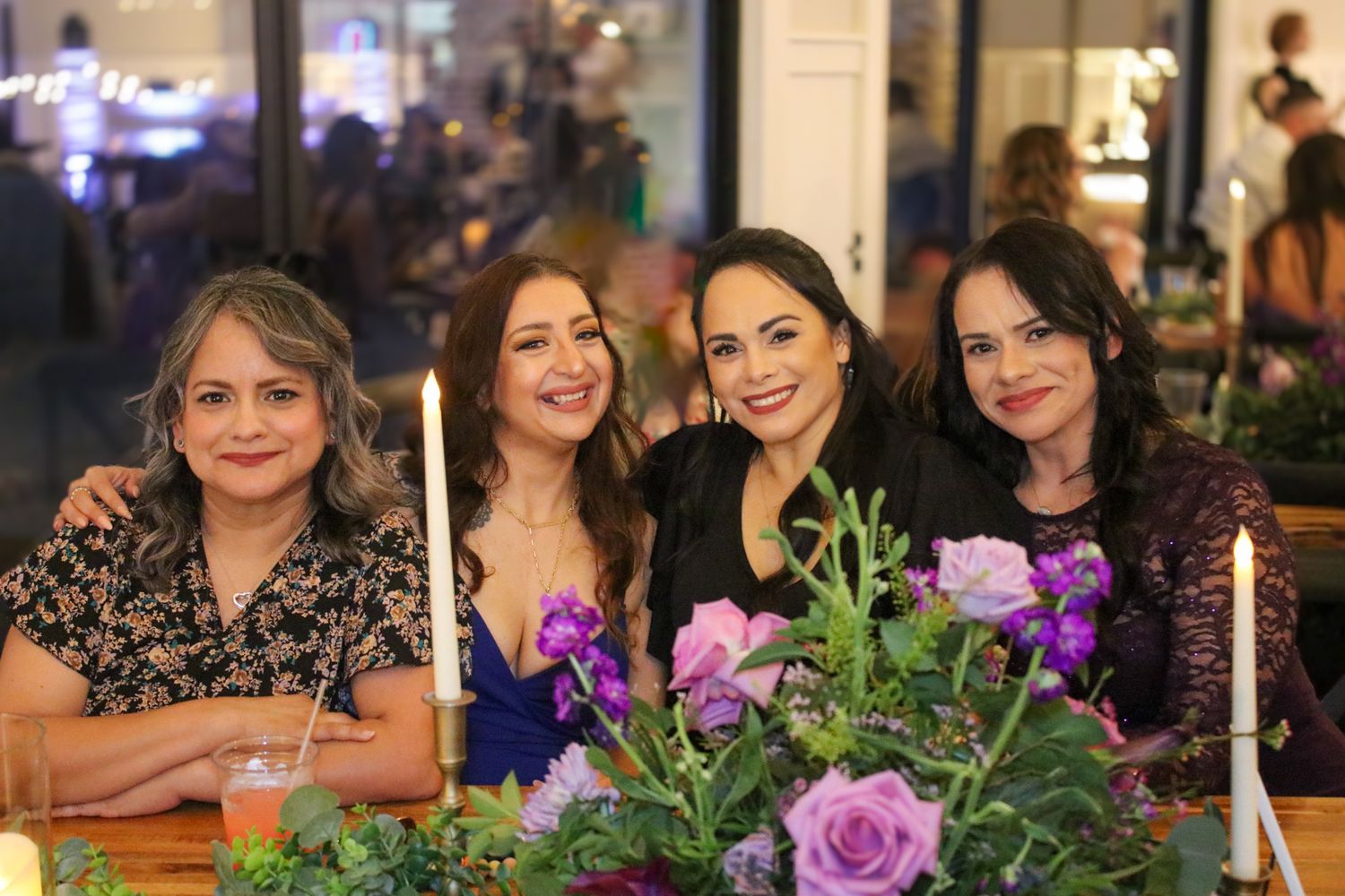 Four friends gather around a table decorated with purple flowers and candles.
