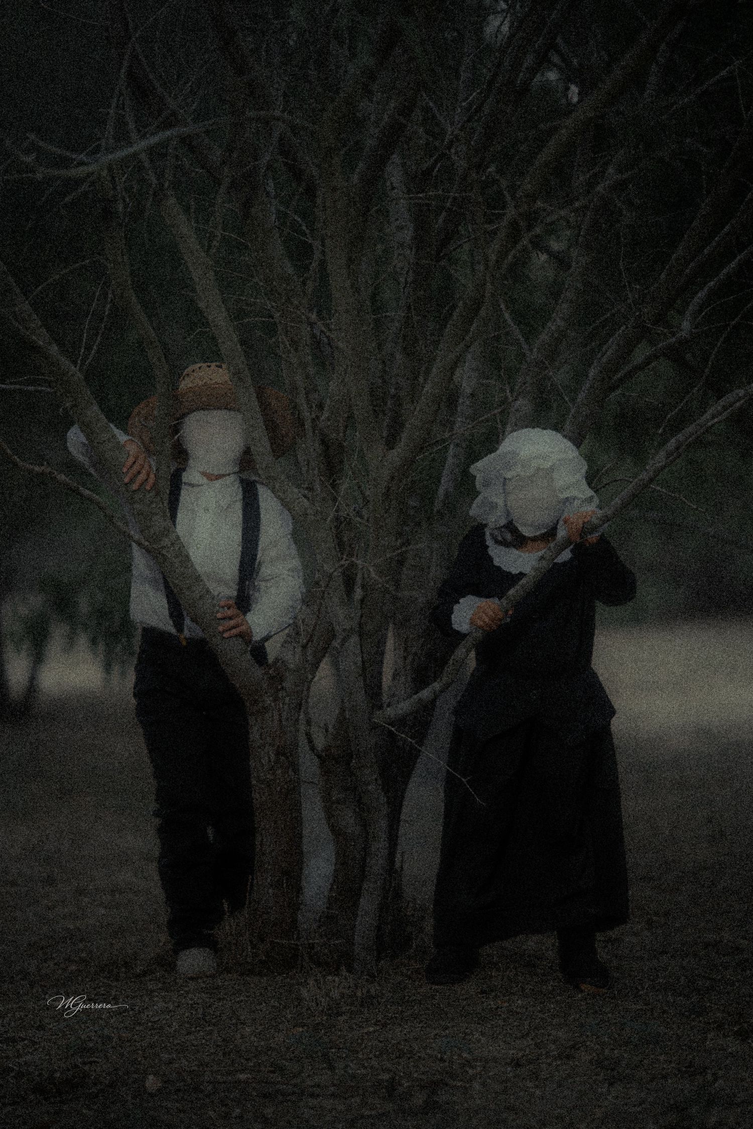 Two faceless figures in dark vintage clothing stand among bare trees in a moody, eerie forest setting.