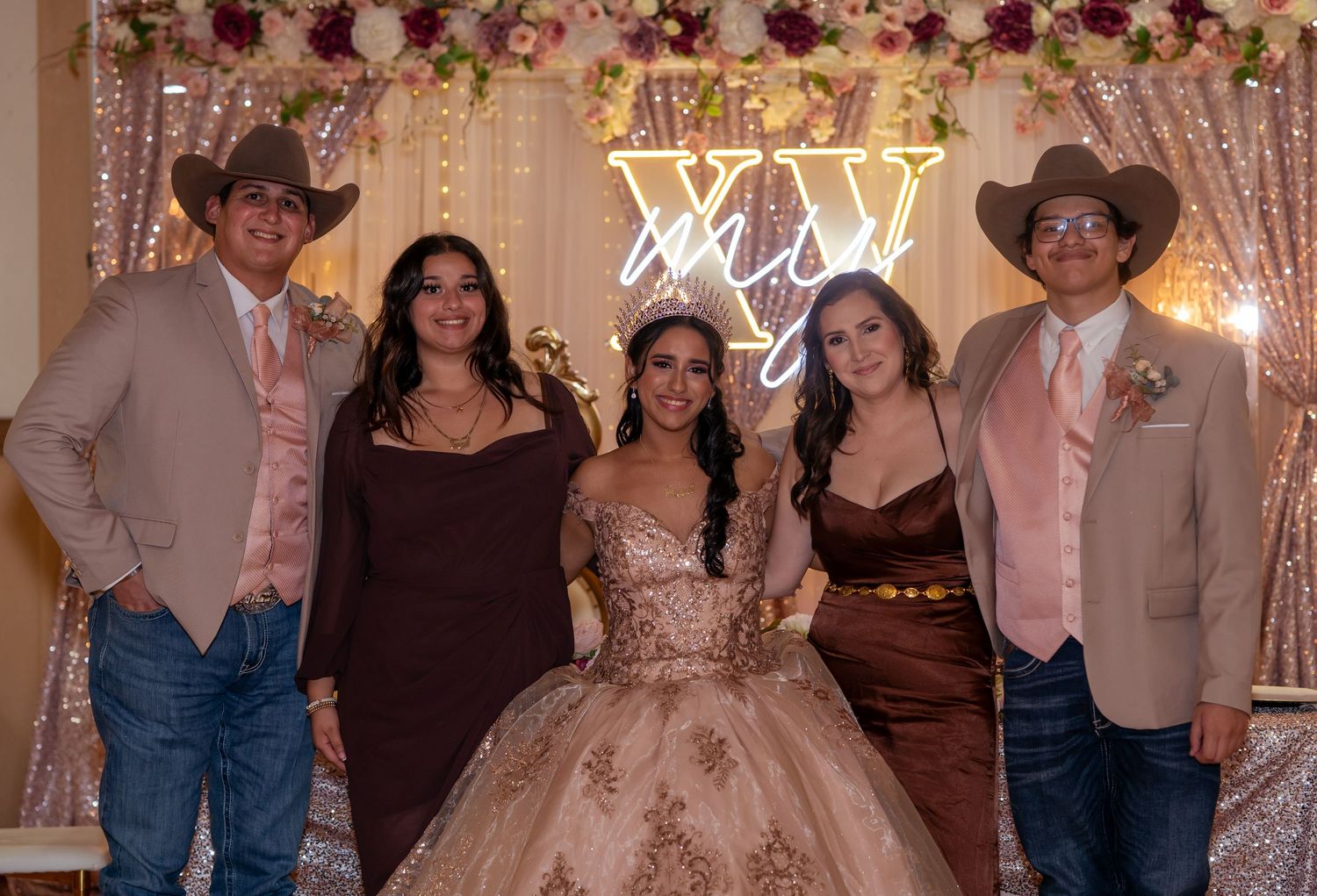 Five elegantly dressed guests pose together at a quinceañera celebration with a glowing XV backdrop.