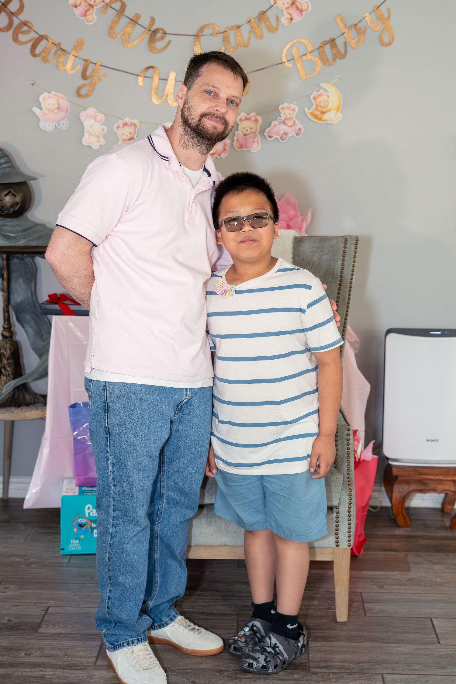 A man and young boy with glasses pose together at a baby shower party with bear-themed decorations.