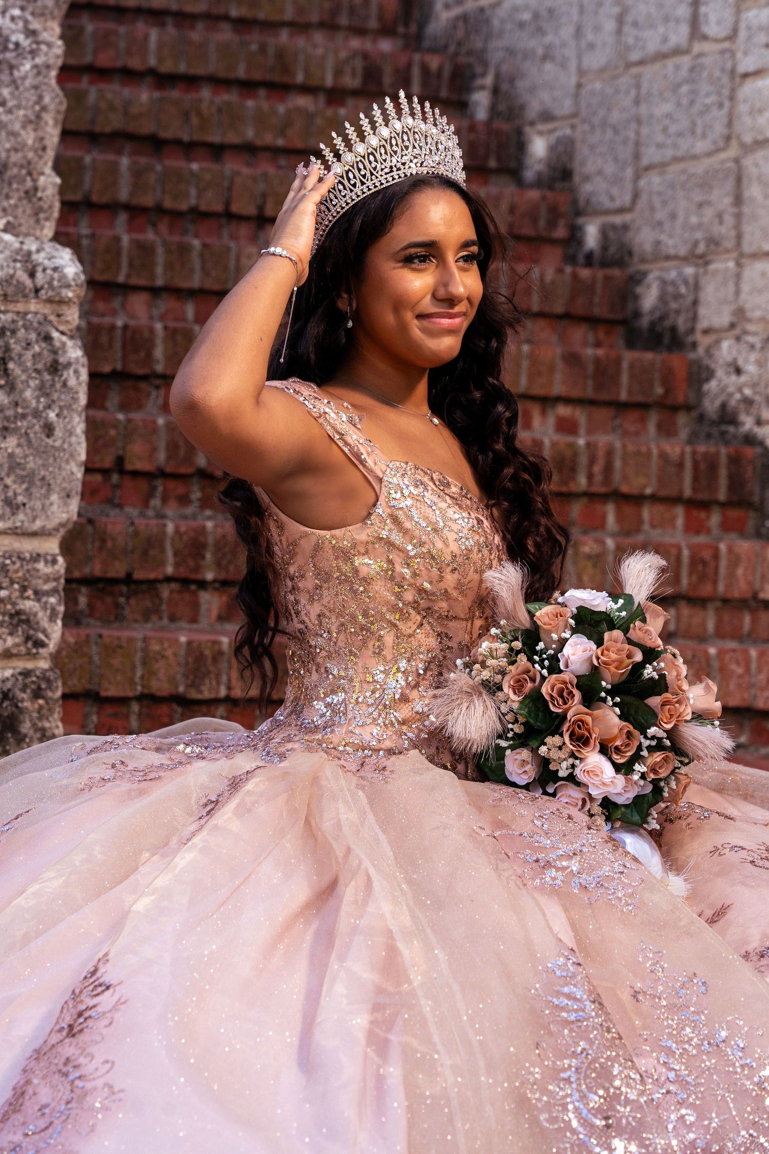 An elegant princess gown in champagne pink with crystal embellishments and matching tiara photographed against stone walls.