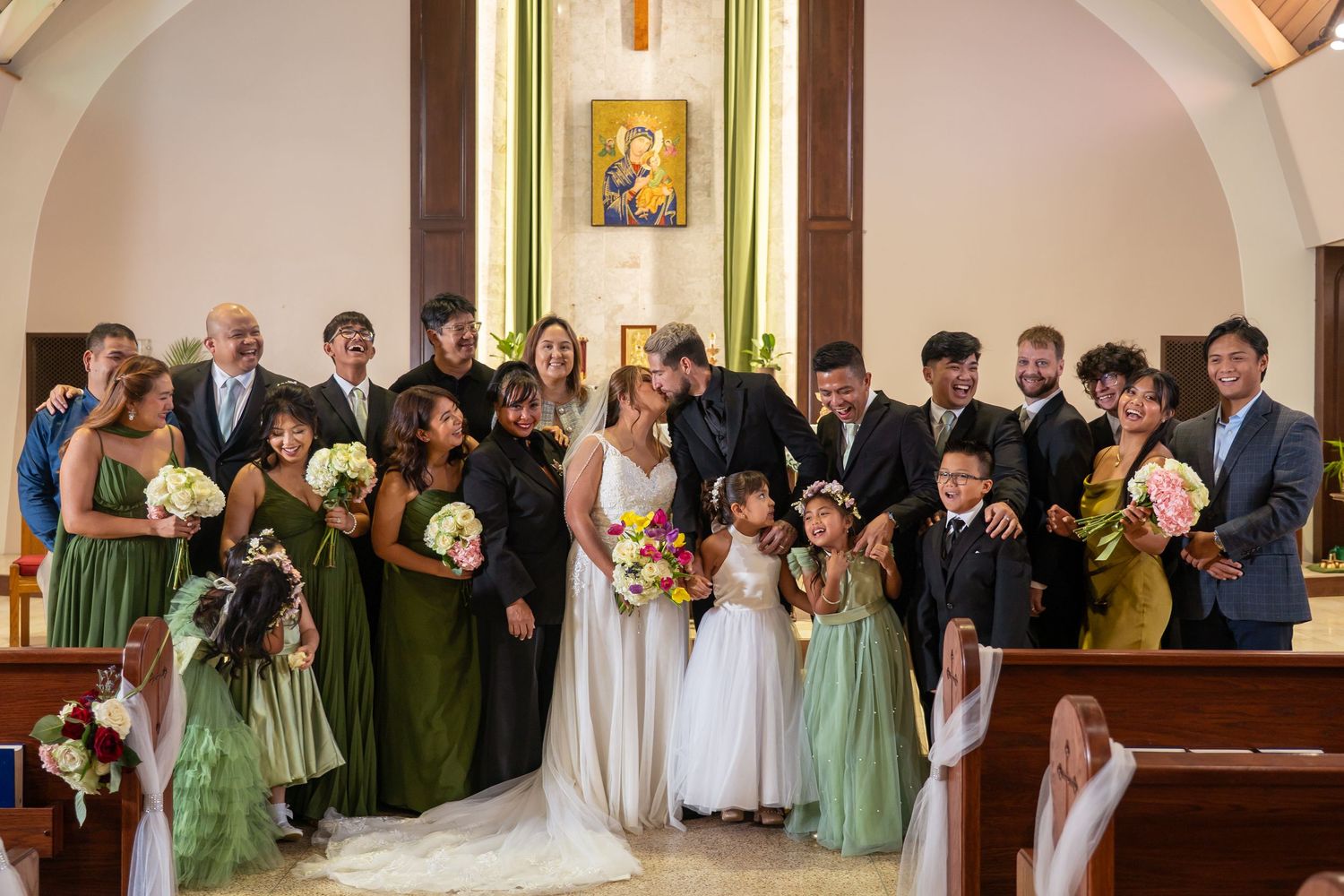 Wedding party and guests stand in a church sanctuary arranged in a panoramic lineup formation during ceremony.