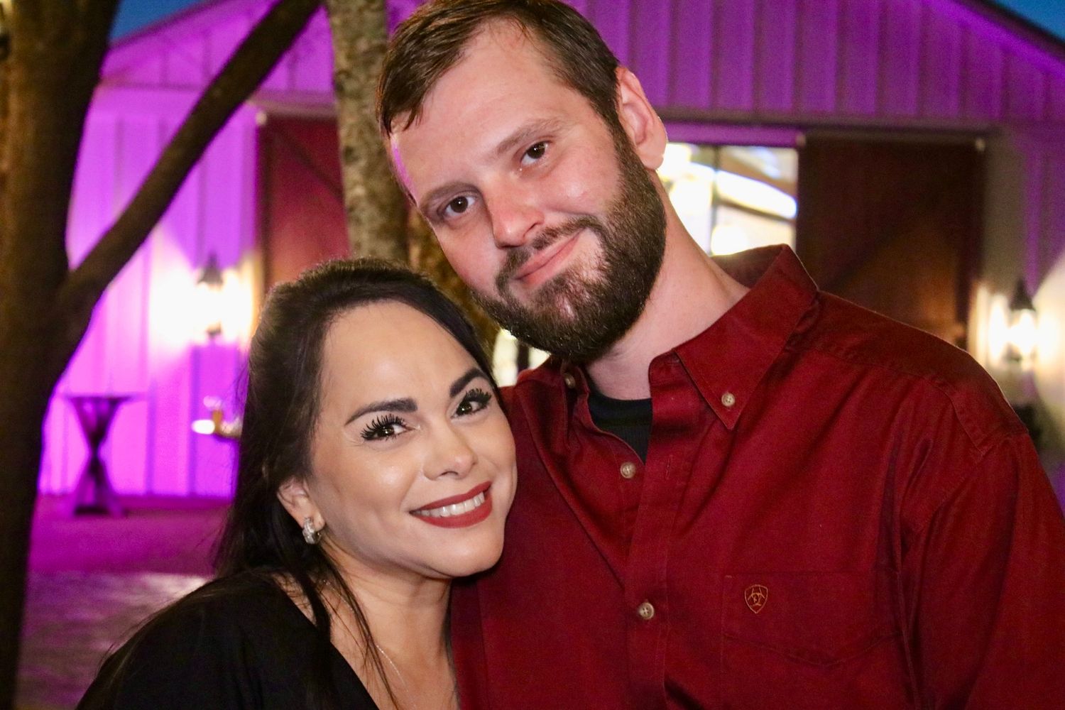 A couple poses together in front of a building with purple lighting.