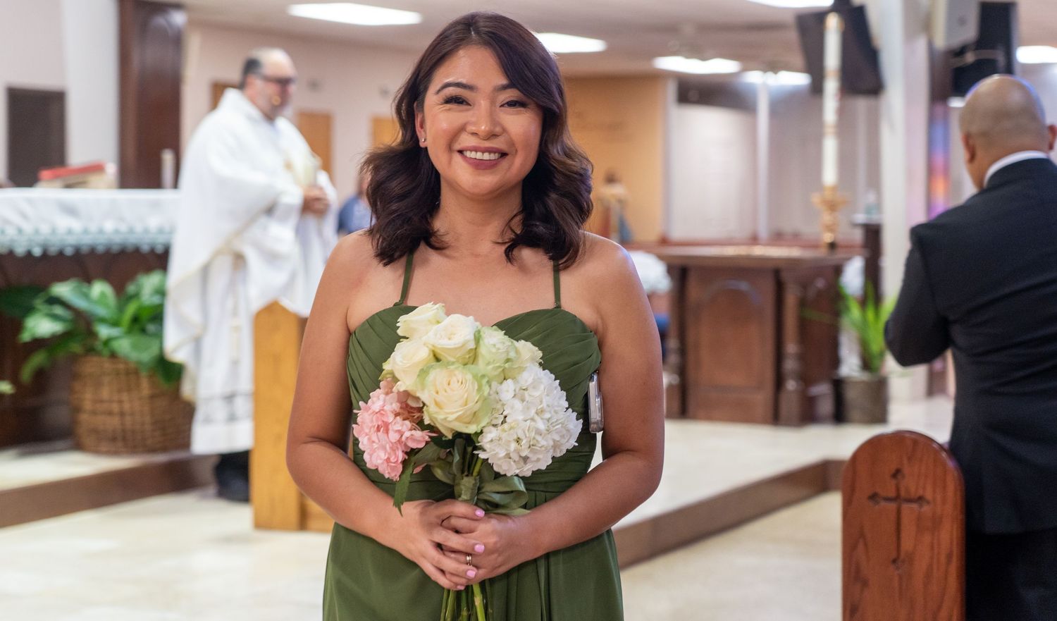 A person holds a bridal bouquet with white and pink flowers in a church setting.