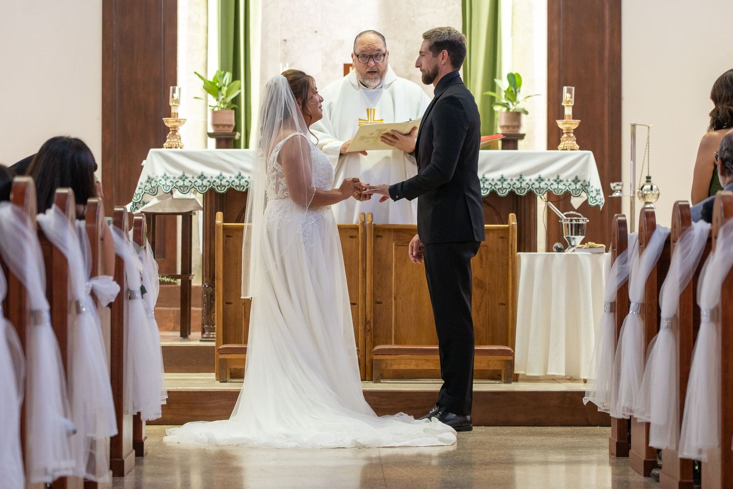 A wedding ceremony in a bright venue with bridesmaids in pink dresses and white floral arrangements.