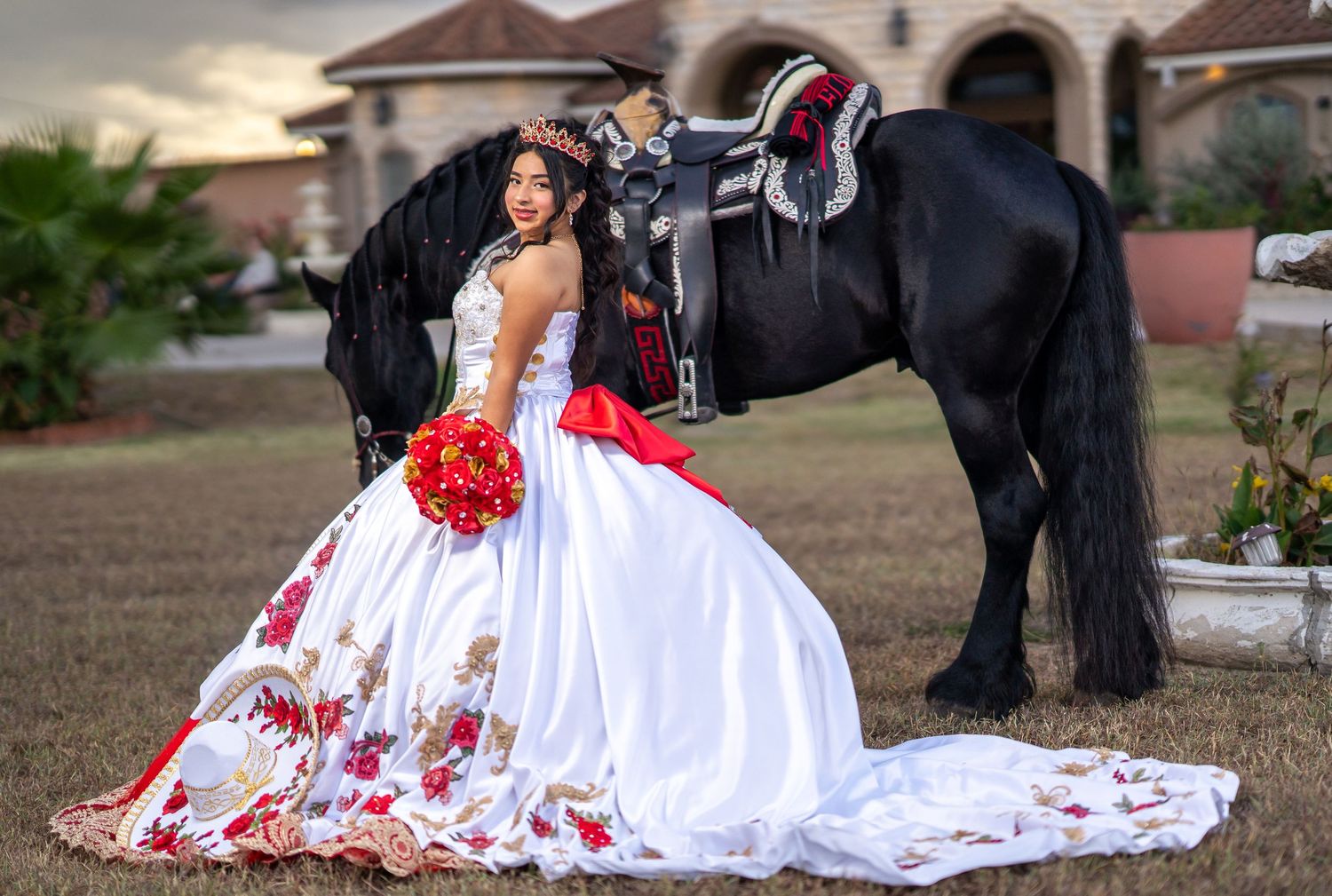 A flowing white dress with red floral accents creates an elegant scene with a black horse.