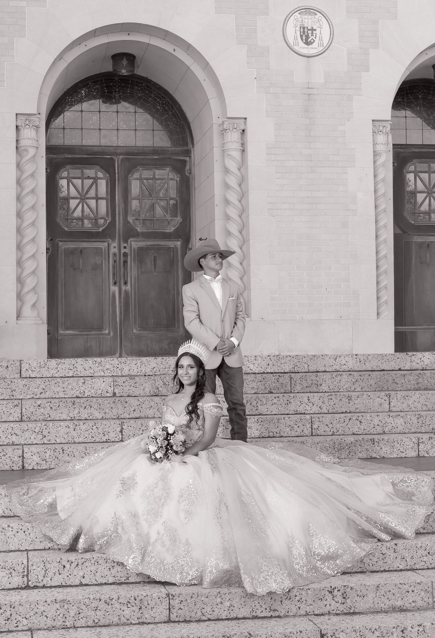 A black and white wedding photo of a couple on church steps with ornate arched doorways in the background.